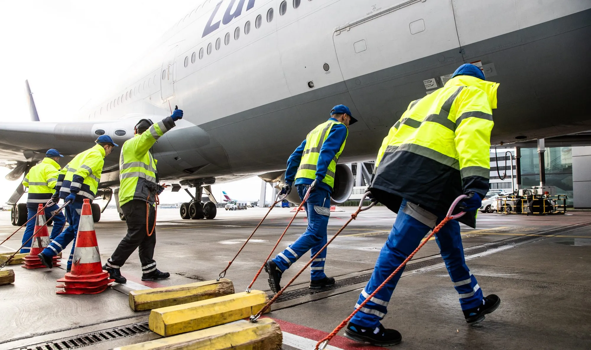 Du siehst eine Fraport-Mitarbeiterin mit Warnweste und Headset lächelnd auf dem Flughafenvorfeld vor einem Flugzeug.