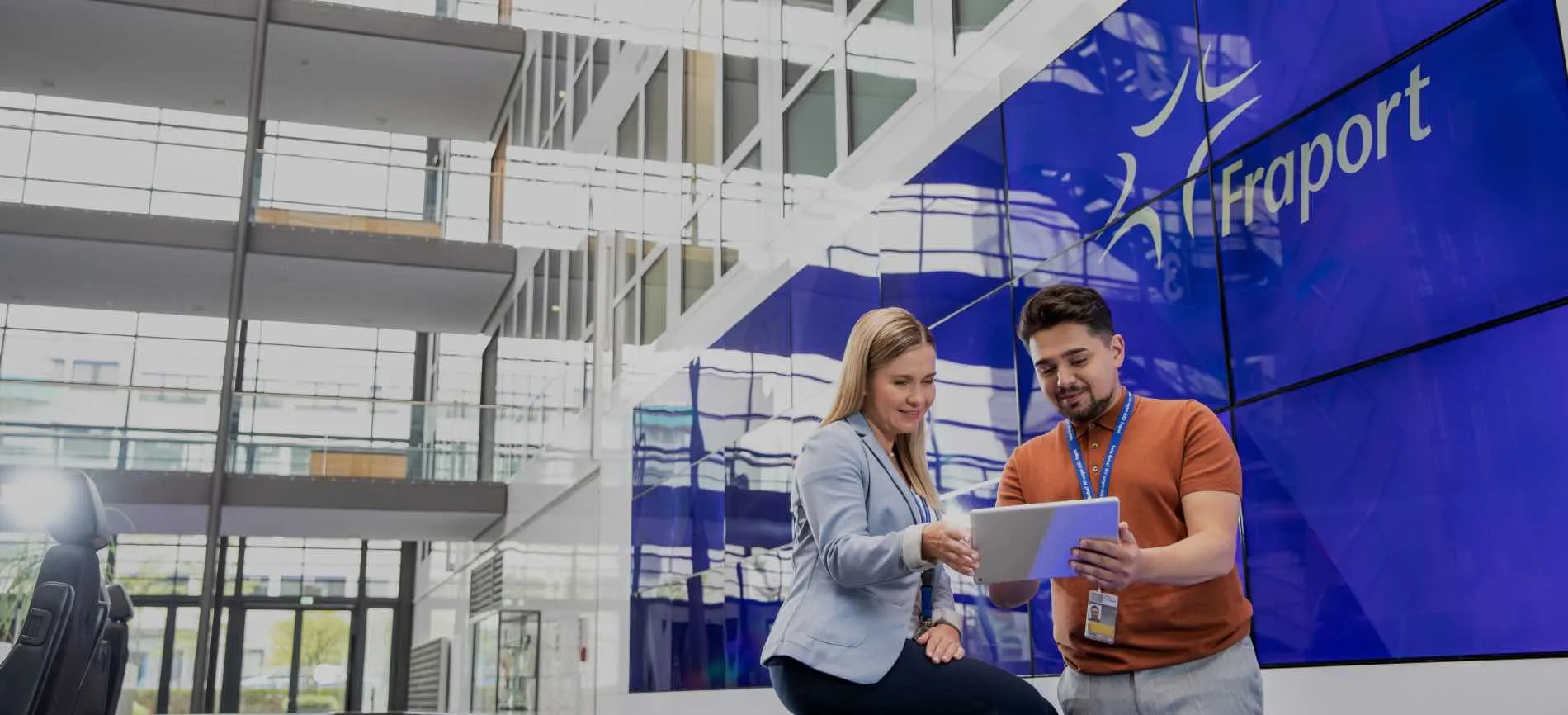 Zwei Mitarbeitende von Fraport schauen gemeinsam auf ein Tablet im modernen Unternehmensgebäude.