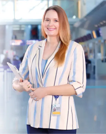 Junge Frau mit Ausweis und Tablet lächelt im modernen Flughafen, bereit für ihren Arbeitstag bei Fraport.