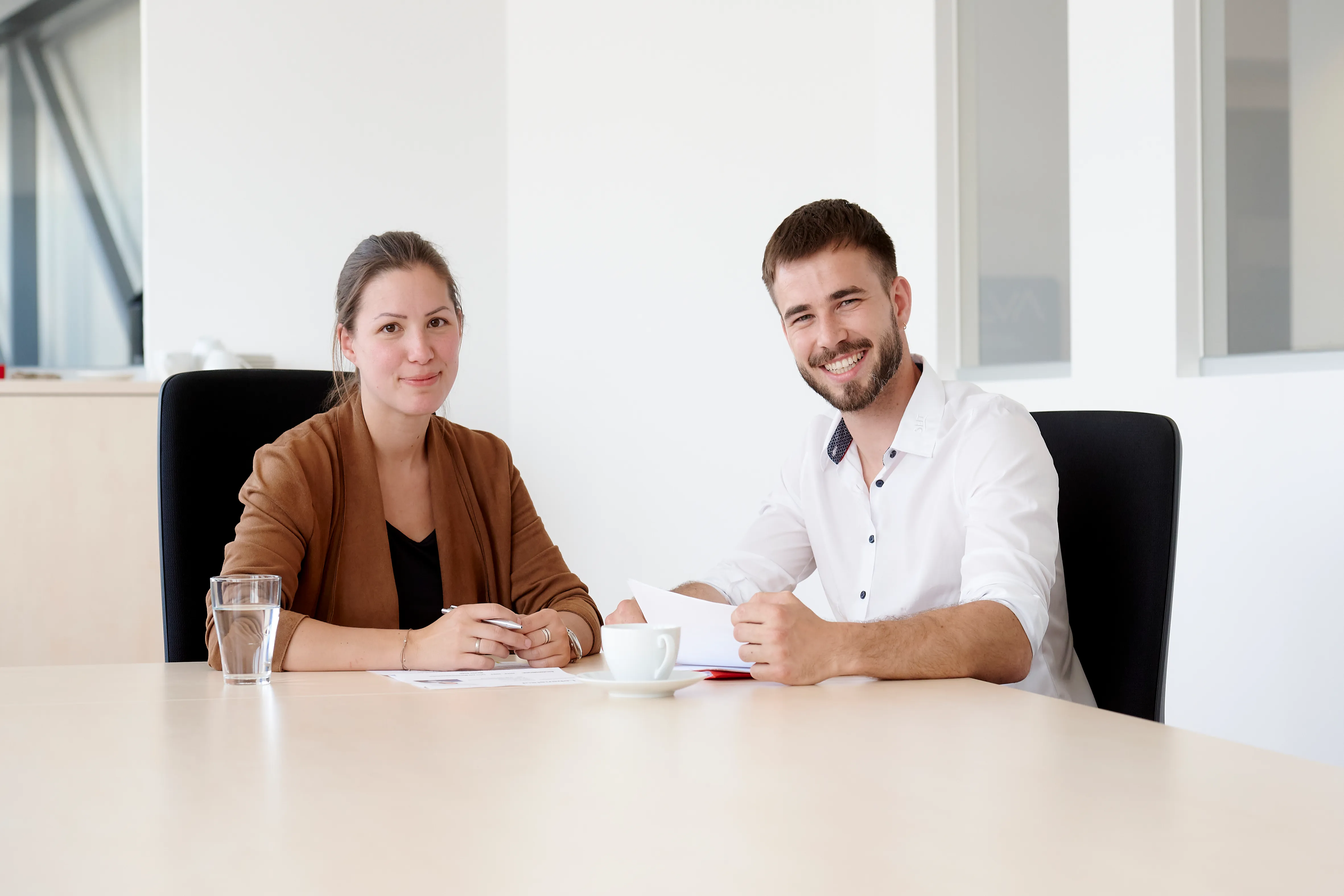 Zwei junge Kollegen sitzen gemeinsam im Büro und besprechen freundlich Bewerbungsunterlagen bei Frauenthal Handel Gruppe.