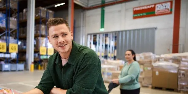 Ein Mitarbeiter lächelt in einem Lager von Fressnapf Holding SE. Im Hintergrund sind Regale und eine Kollegin zu sehen.