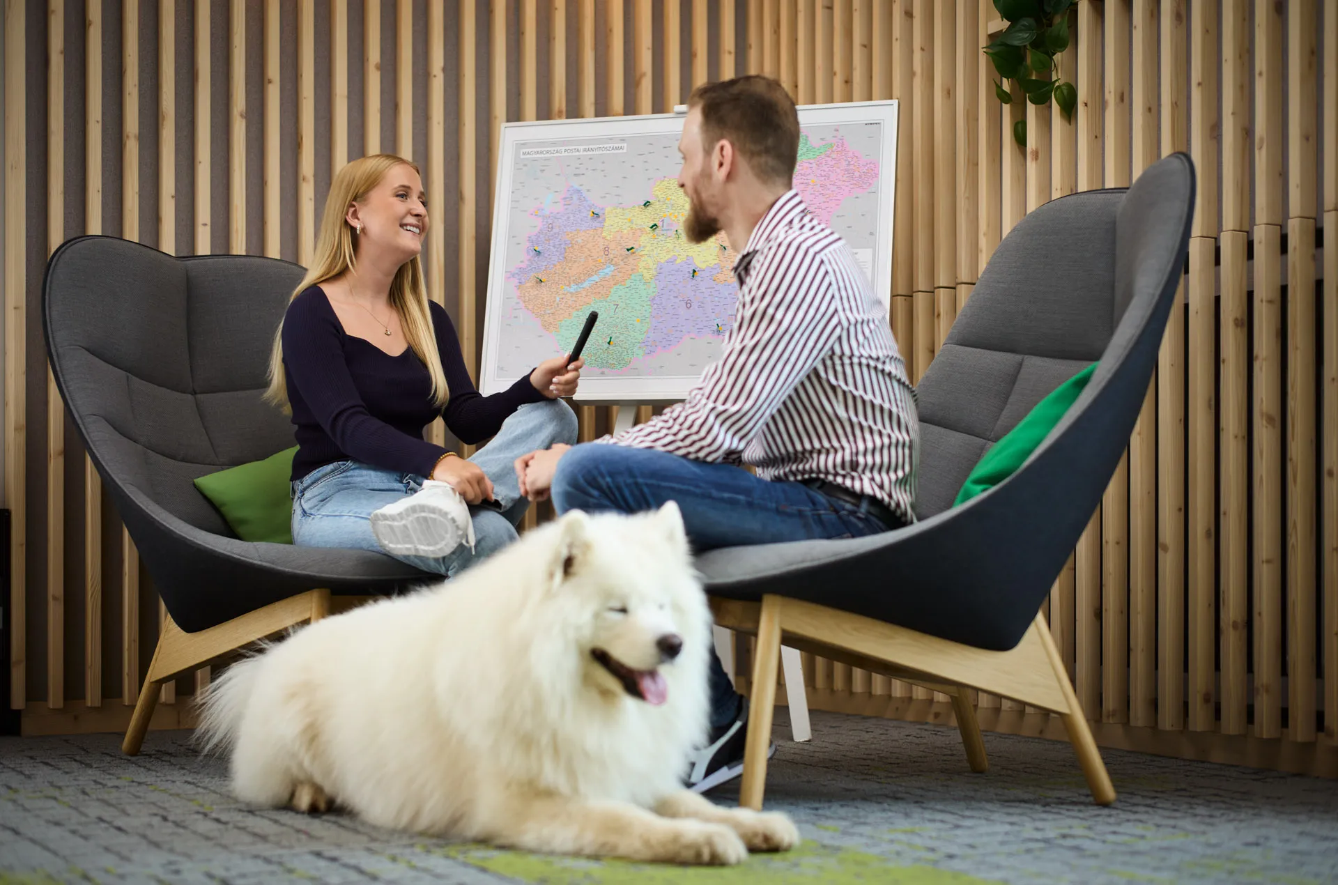 Zwei Personen unterhalten sich im Büro von Fressnapf, mit einer Landkarte im Hintergrund und einem Hund im Vordergrund.