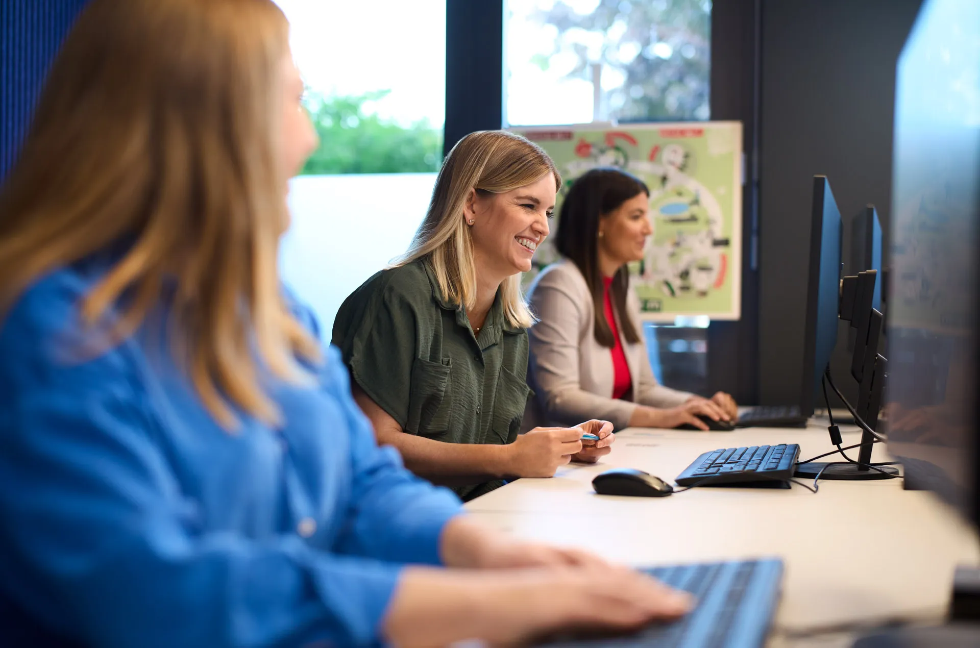 Drei Personen sitzen lächelnd an Computern in einem modernen Büro bei Fressnapf Holding SE.