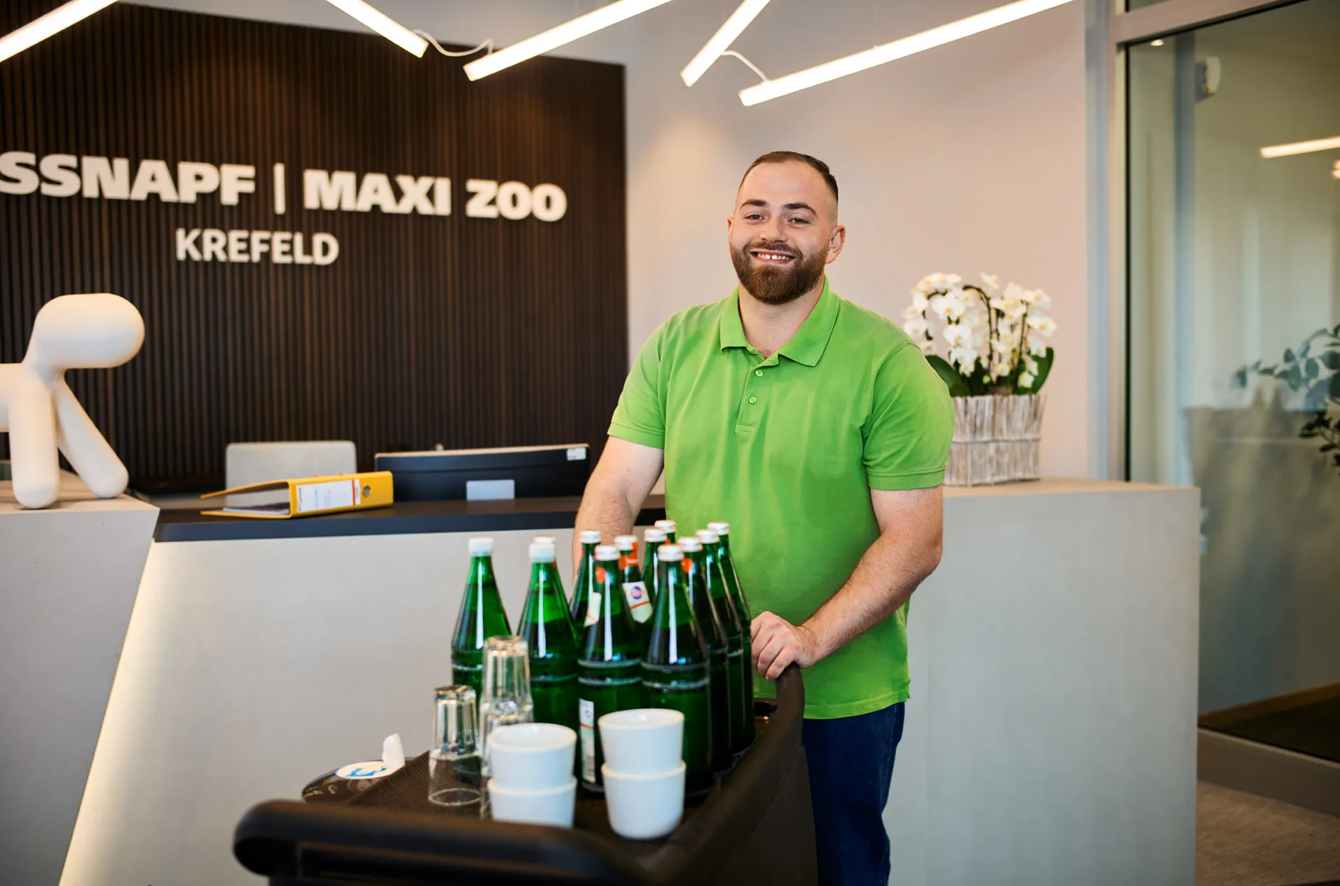 Ein lächelnder Mitarbeiter im grünen Polohemd steht an der Rezeption von Fressnapf Krefeld.