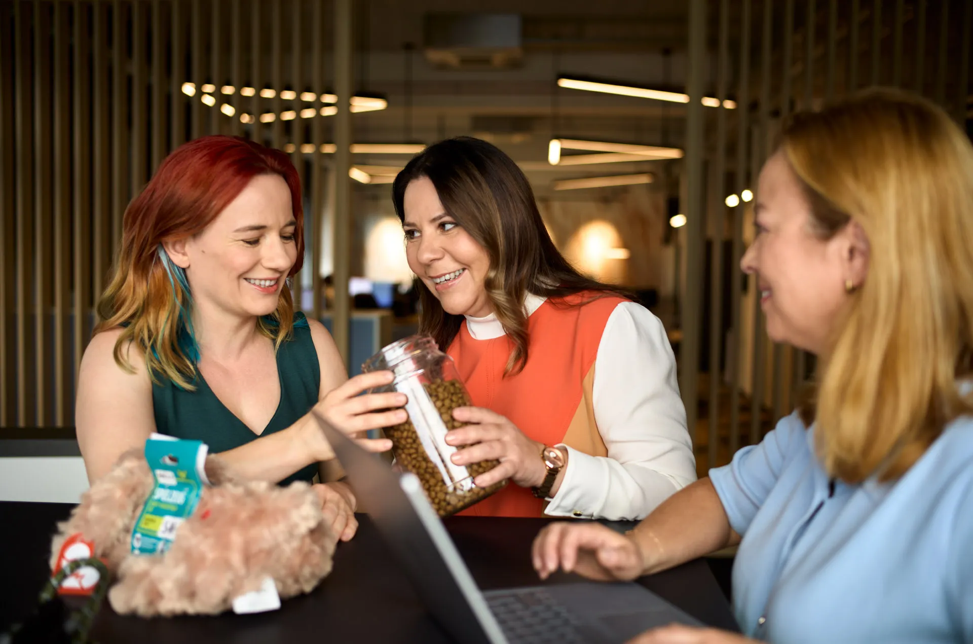 Drei Frauen unterhalten sich fröhlich über ein Glas mit Tierfutter in einem modernen Büro.