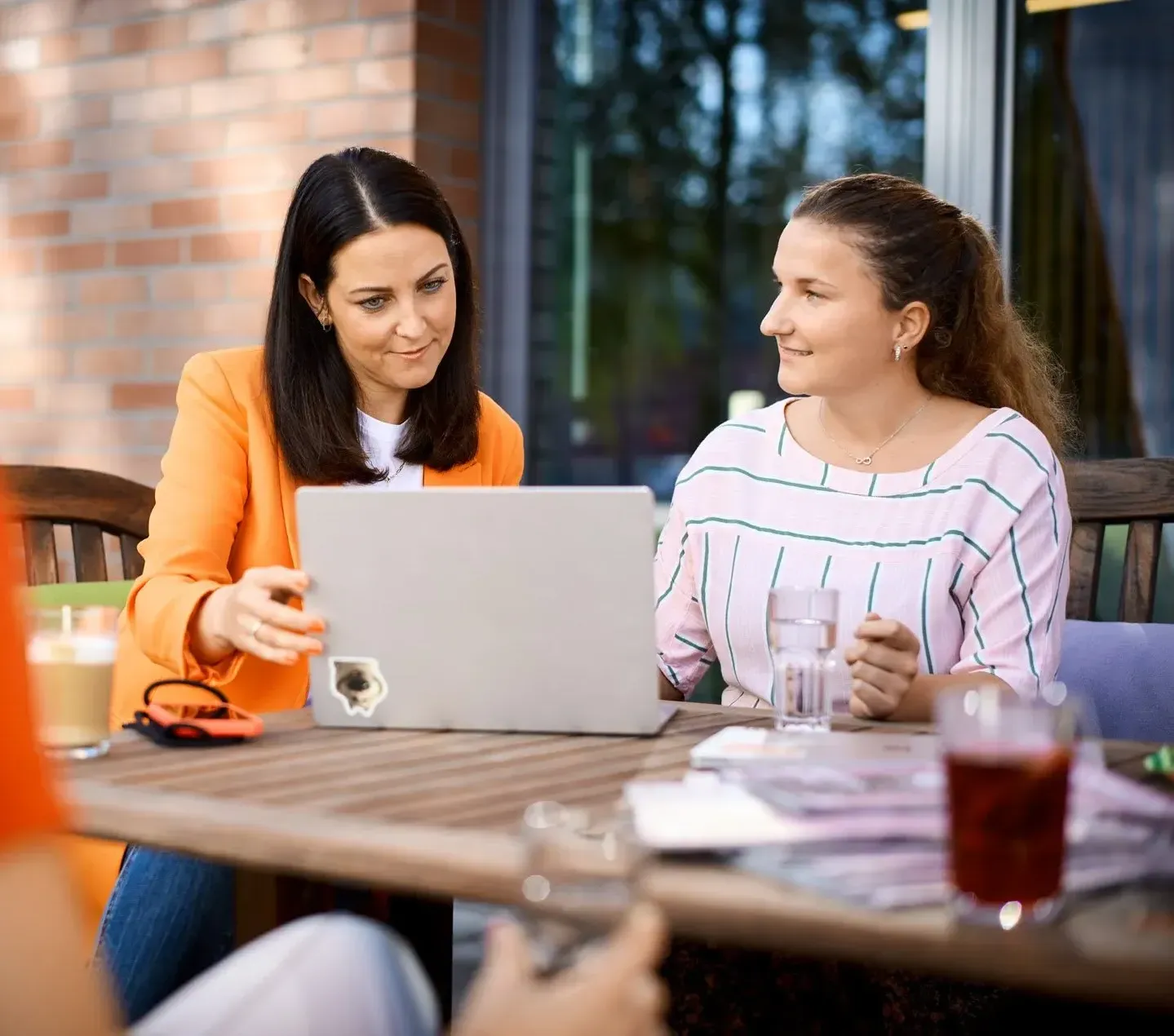 Drei Frauen sitzen draußen an einem Tisch, diskutieren freundlich und schauen auf einen Laptop.
