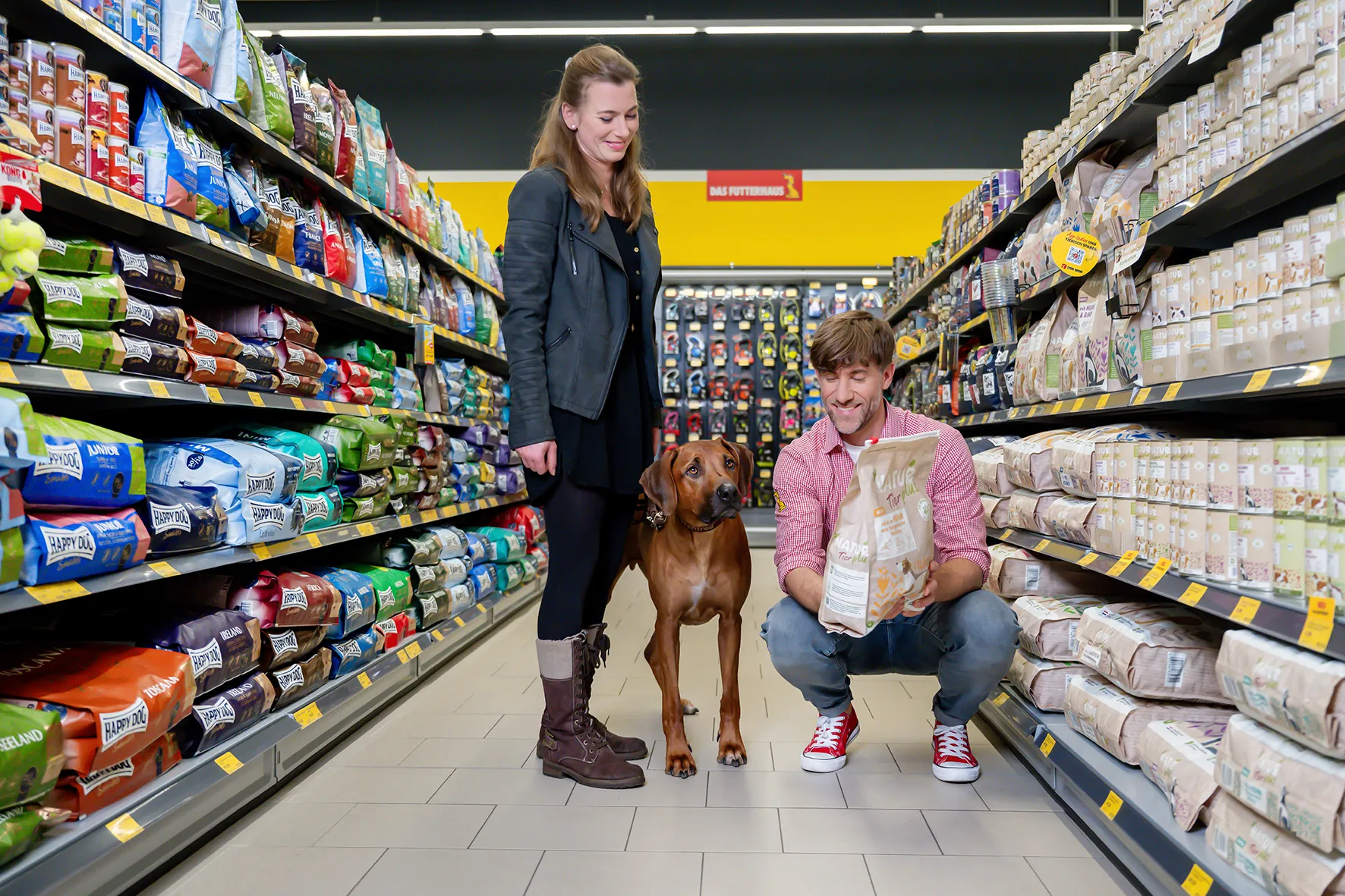 Zwei Menschen mit Hund im Das Futterhaus, Du wählst gemeinsam passendes Hundefutter im Laden aus.