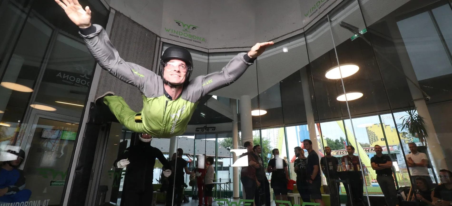 Ein Mitarbeiter von Gepardec schwebt beim Indoor Skydiving, während Kollegen begeistert zuschauen.
