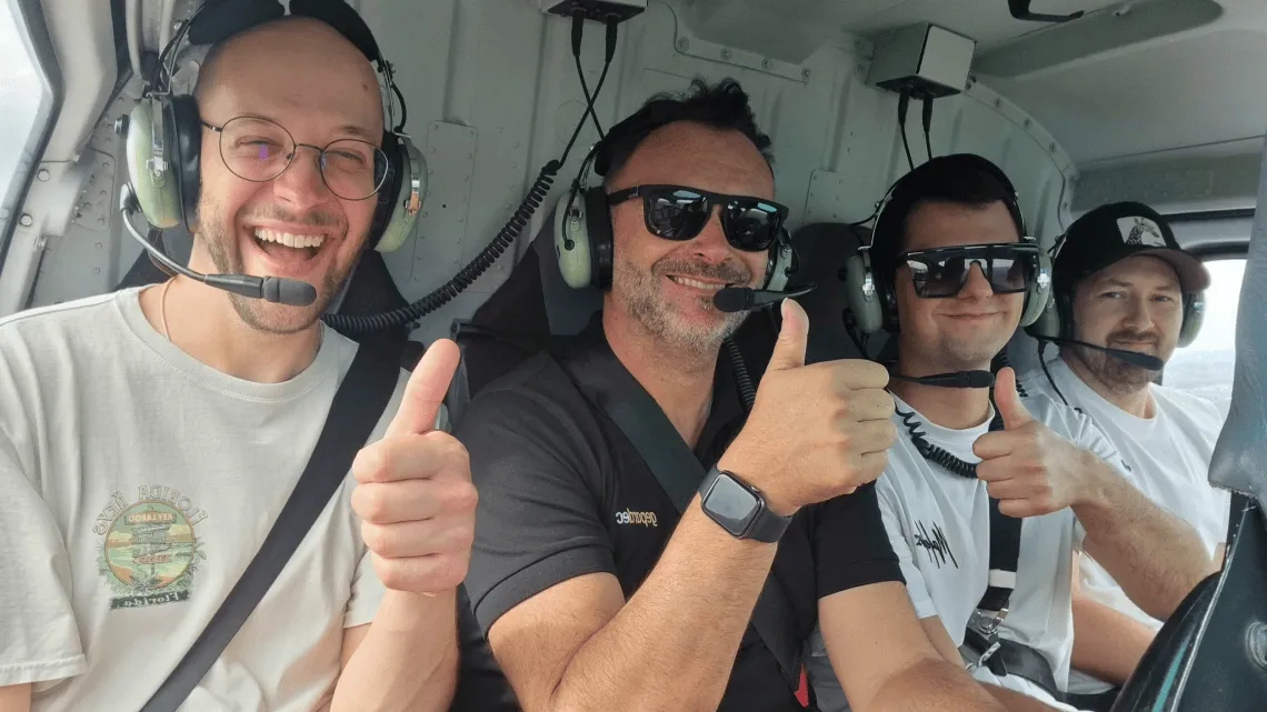 Vier gut gelaunte IT-Kollegen von Gepardec im Helikopter zeigen Dir mit Daumen hoch Teamgeist und Abenteuerlust.