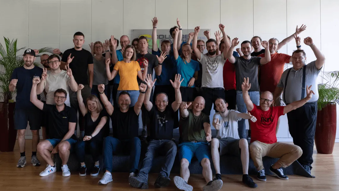 Ein fröhliches Team von Gepardec IT Services posiert gemeinsam, lacht und streckt die Arme in die Höhe.