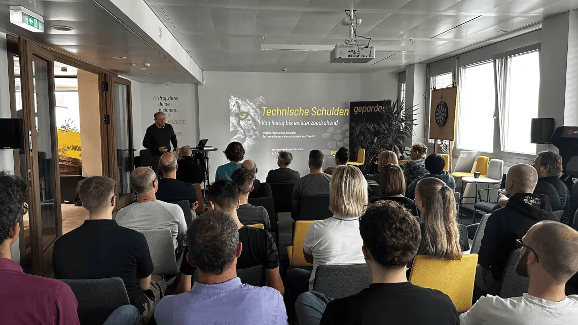 Ein IT-Experte hält bei Gepardec einen Vortrag zum Thema technische Schulden vor aufmerksamem Publikum im modernen Büro.