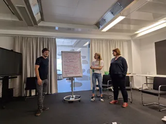 Drei Kolleg:innen präsentieren gemeinsam Ideen auf einem Flipchart in einem modernen IT-Büro von Gepardec.