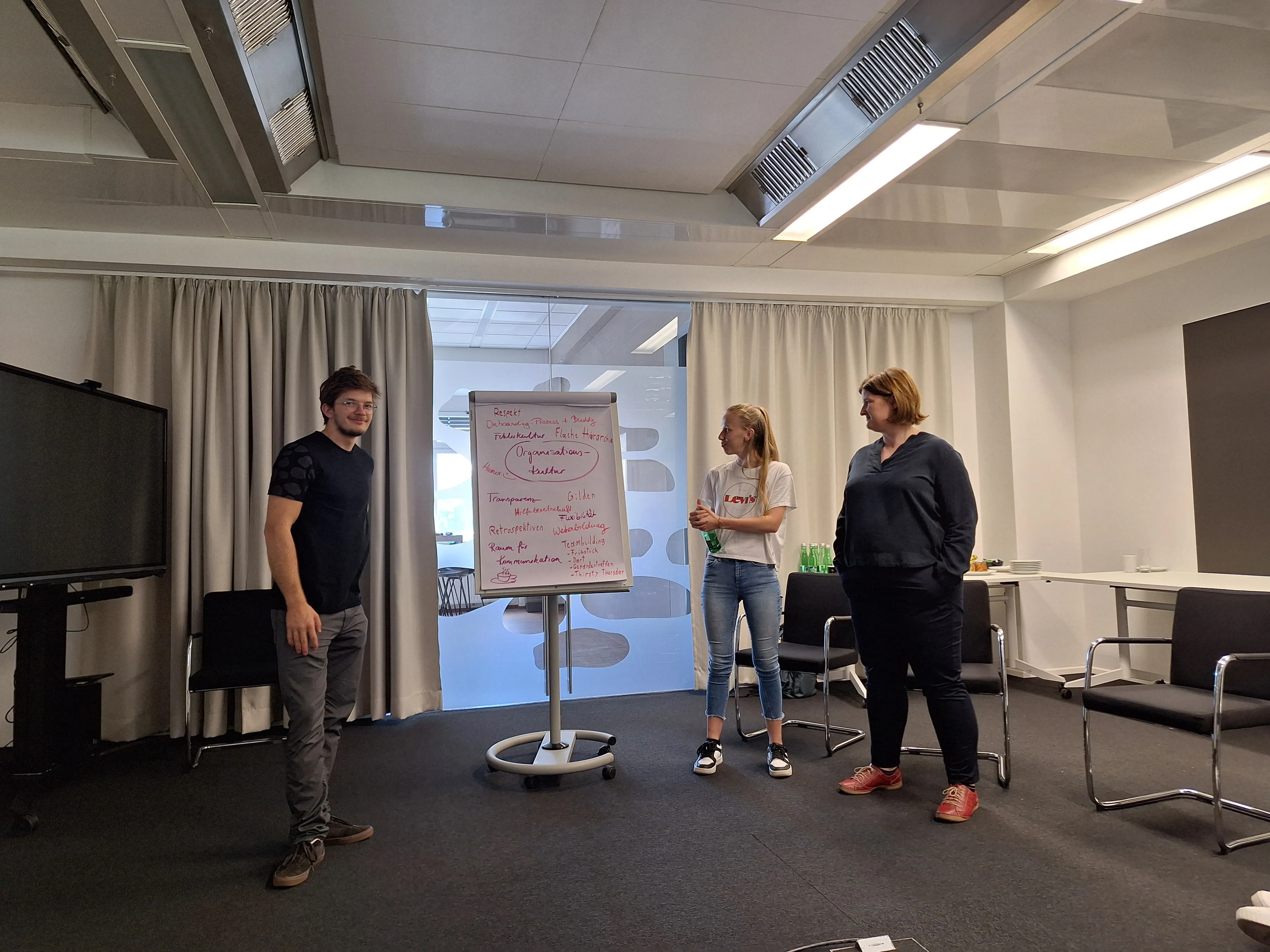 Drei Kolleg:innen präsentieren gemeinsam Ideen auf einem Flipchart in einem modernen IT-Büro von Gepardec.