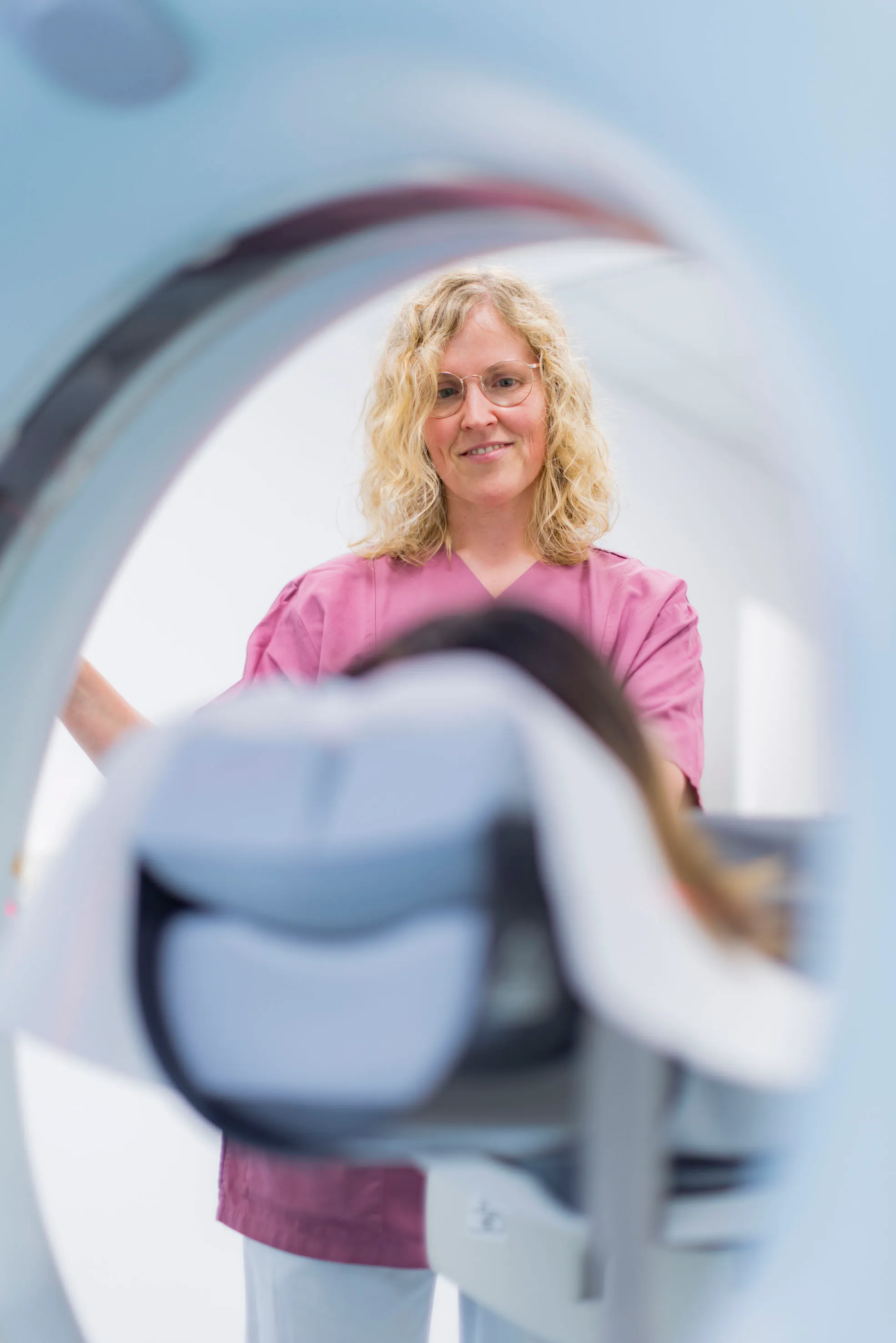 Eine Mitarbeiterin in pinker Kleidung betreut eine Patientin bei einer Untersuchung im MRT-Gerät.