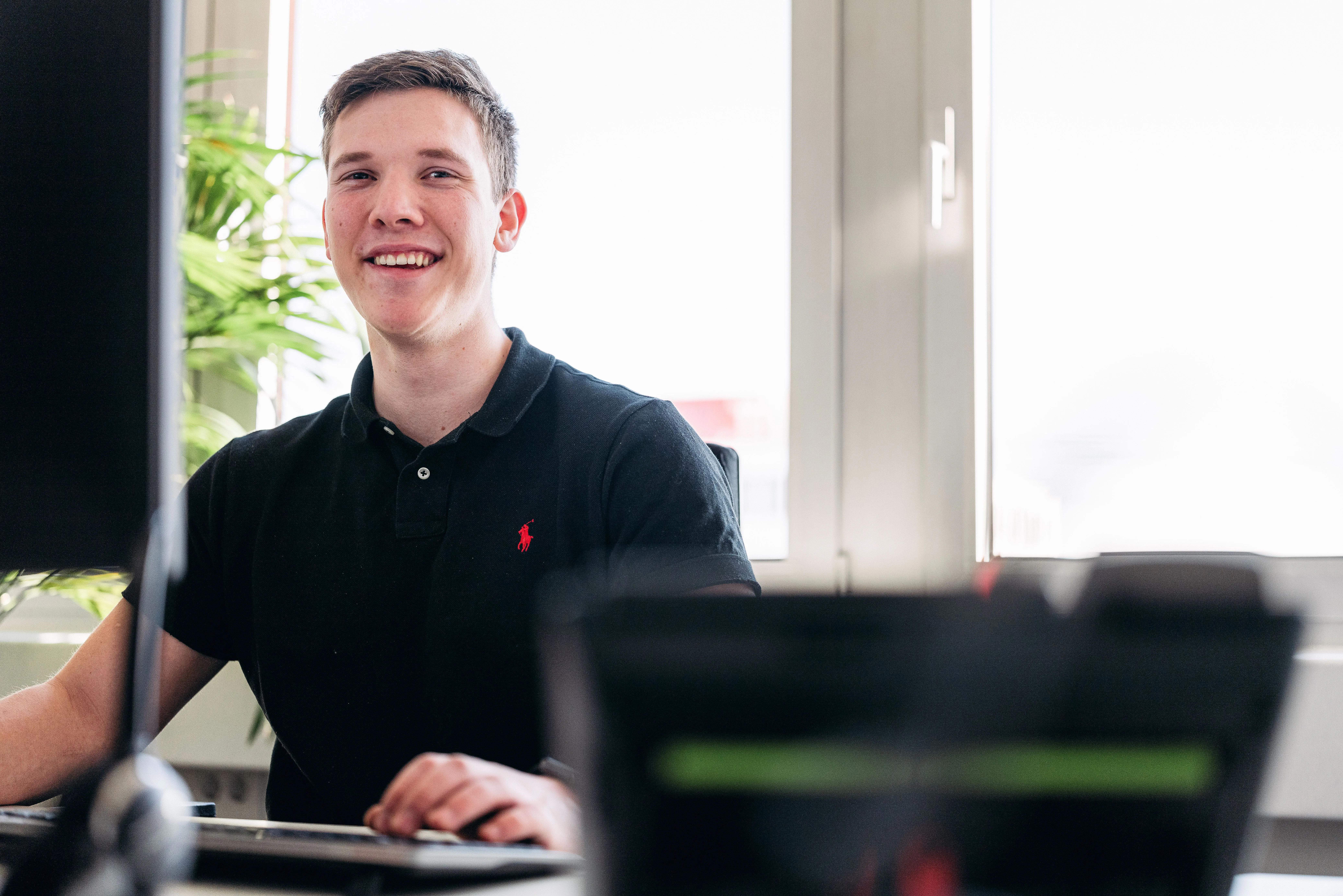 Eine Frau arbeitet an einem Schreibtisch mit Computer im Büro der GTÜ, im Hintergrund eine Kollegin mit Headset.