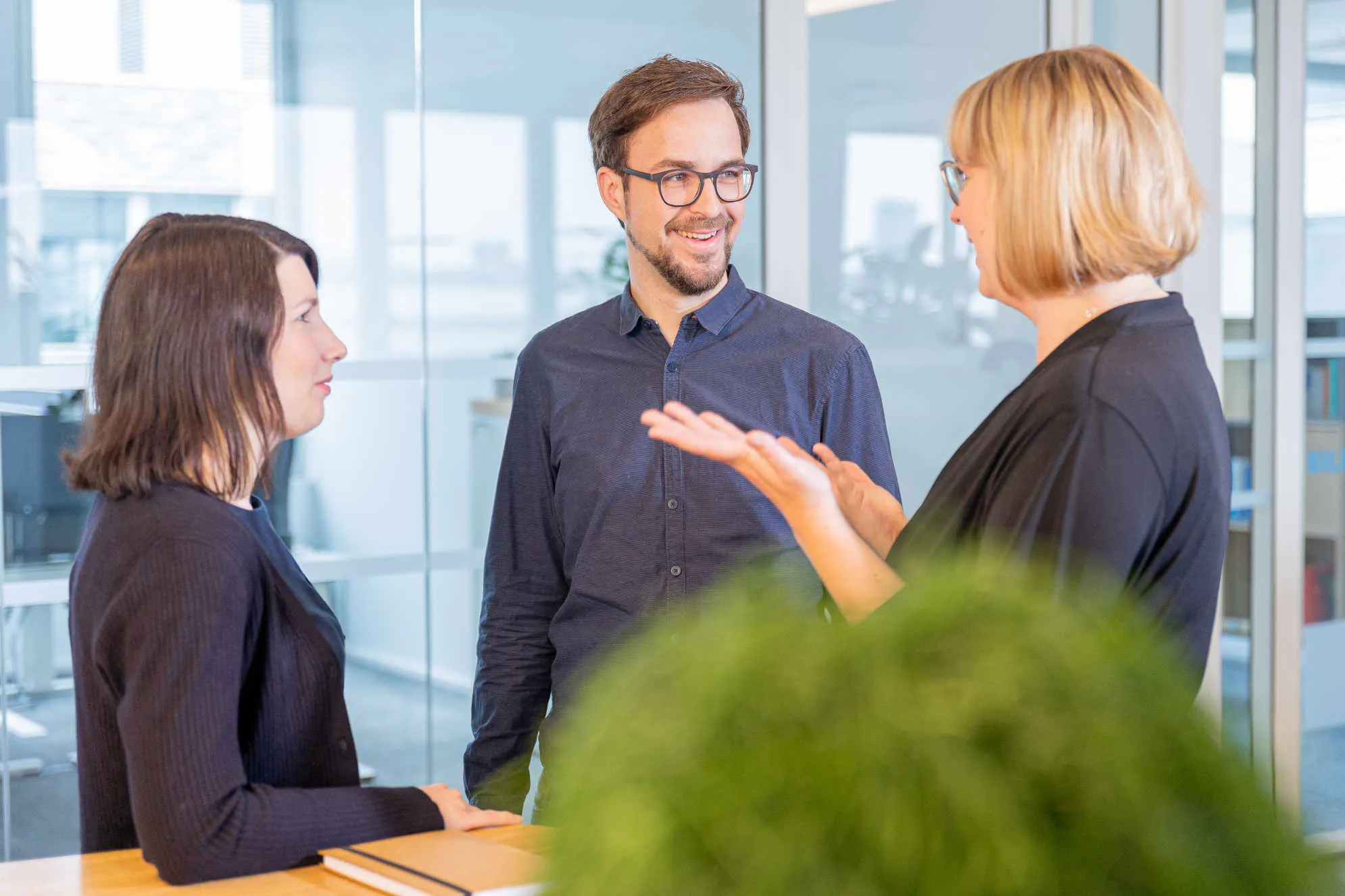 Drei Kolleg:innen von GWQ ServicePlus AG hören aufmerksam einer Präsentation im modernen Büro zu.
