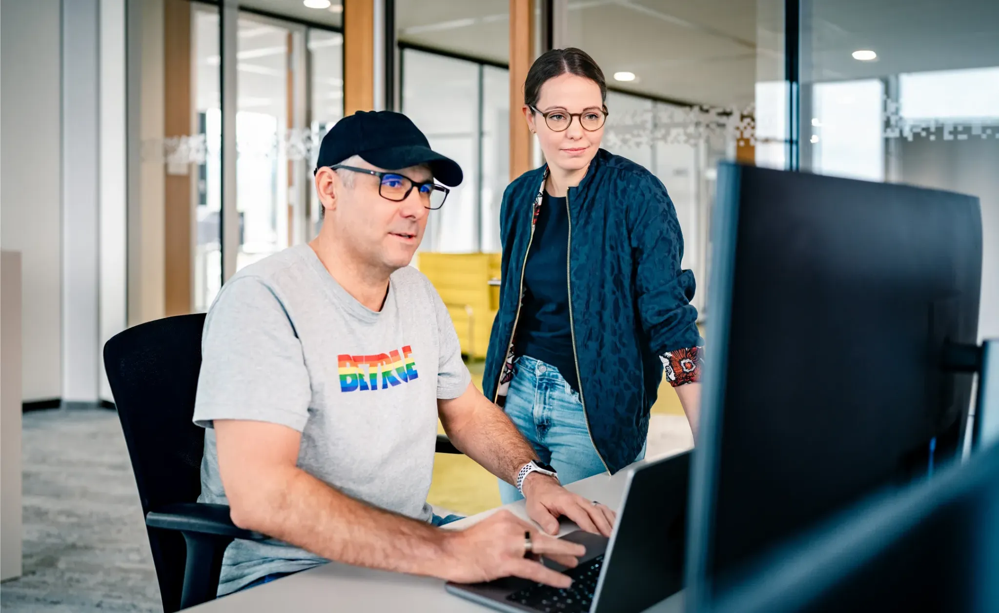 Ein Mann und eine Frau arbeiten gemeinsam an einem Laptop in einem modernen Büro bei Haufe-Group.
