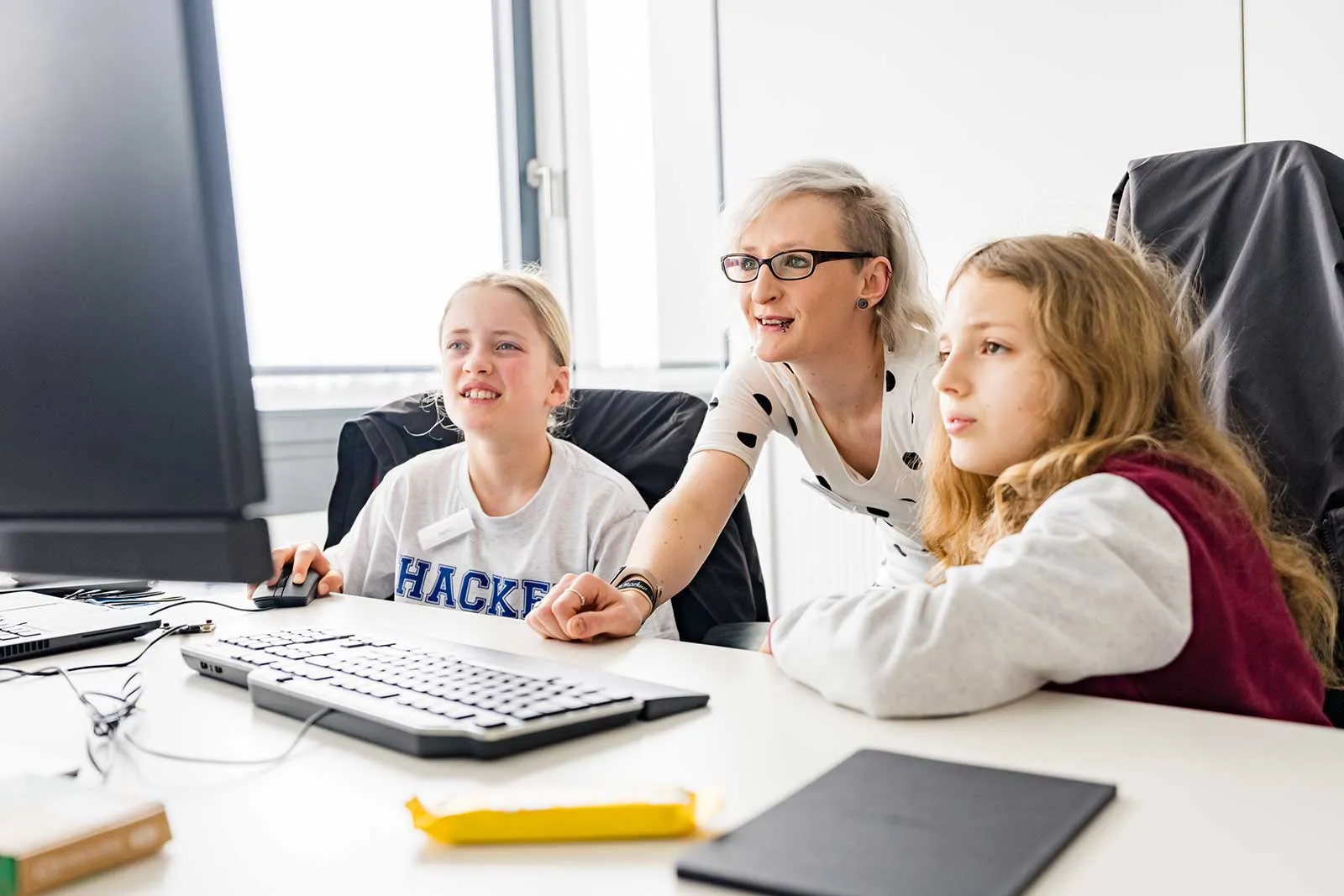 Mentorin erklärt zwei jungen Mädchen etwas am Computer.