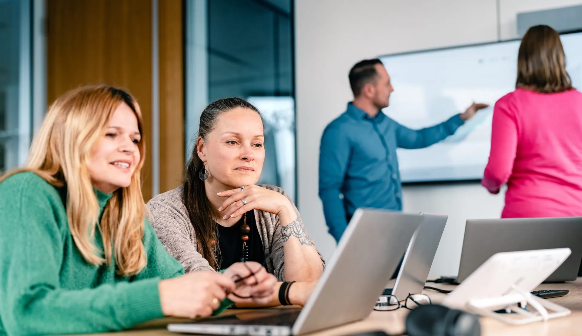 Two colleagues focused on laptops and another presenting at a screen