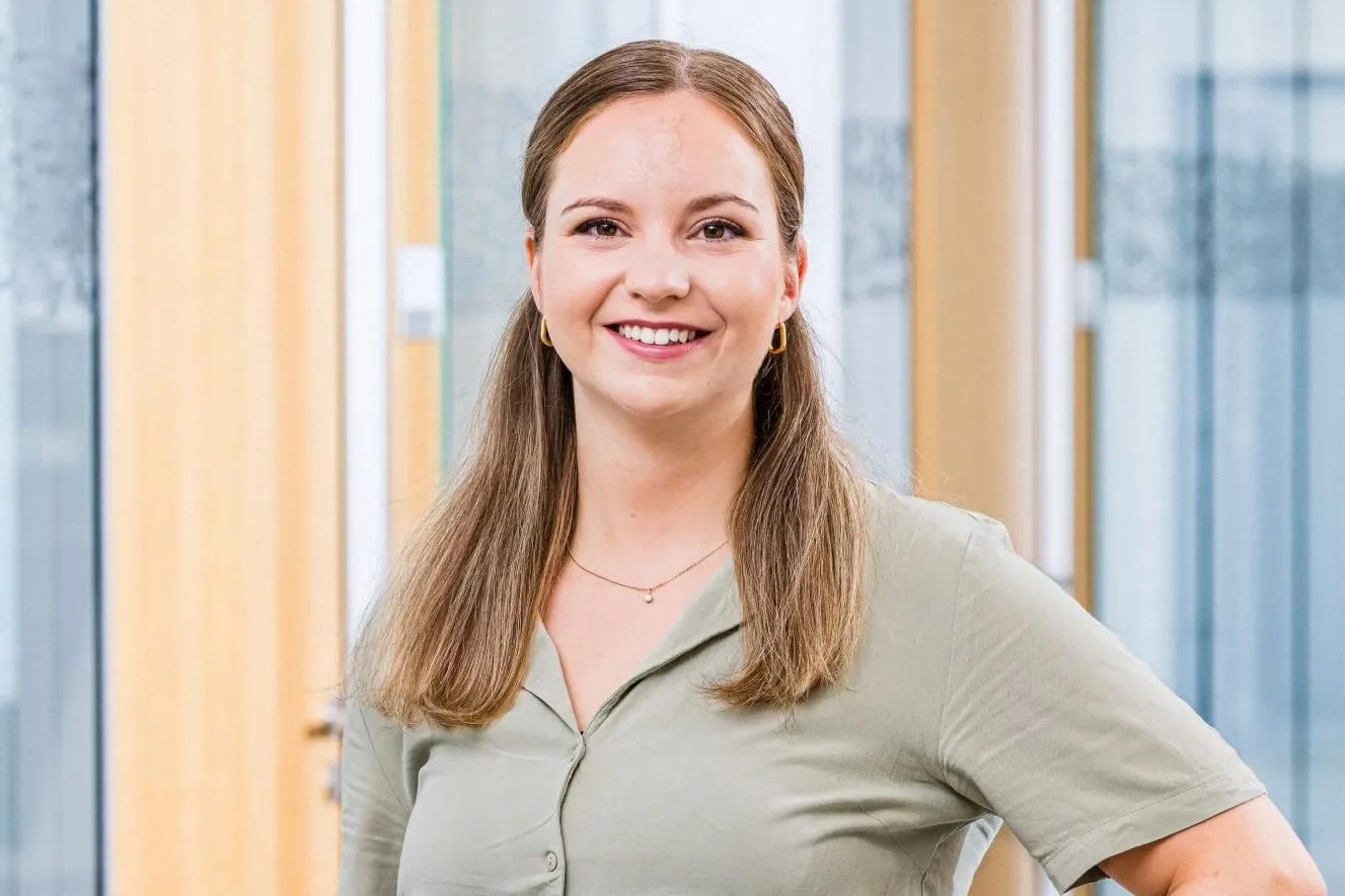 A smiling woman stands confidently in a modern office hallway at the Haufe Group.