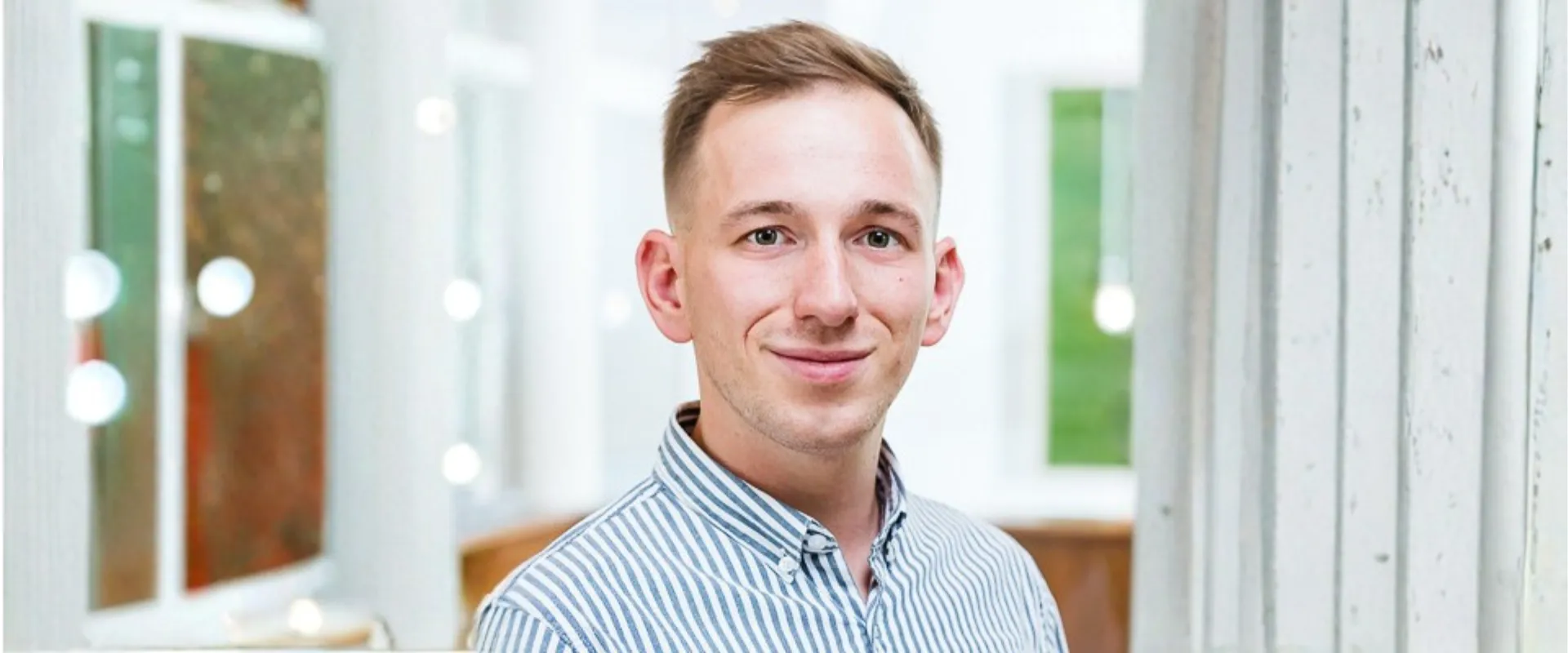 Ein lächelnder junger Mann in einem Büro mit hellem Hintergrund.