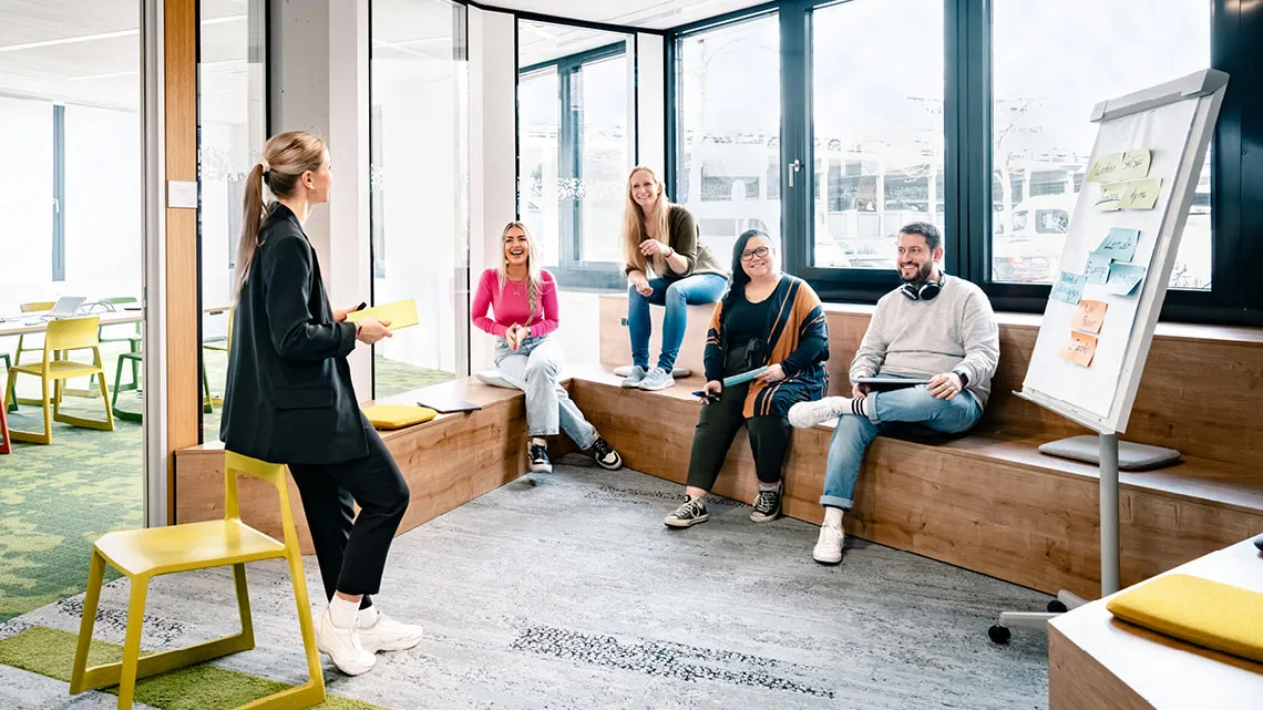 Eine Gruppe junger IT-Profis diskutiert in einem modernen Büro. Eine Frau präsentiert am Flipchart.