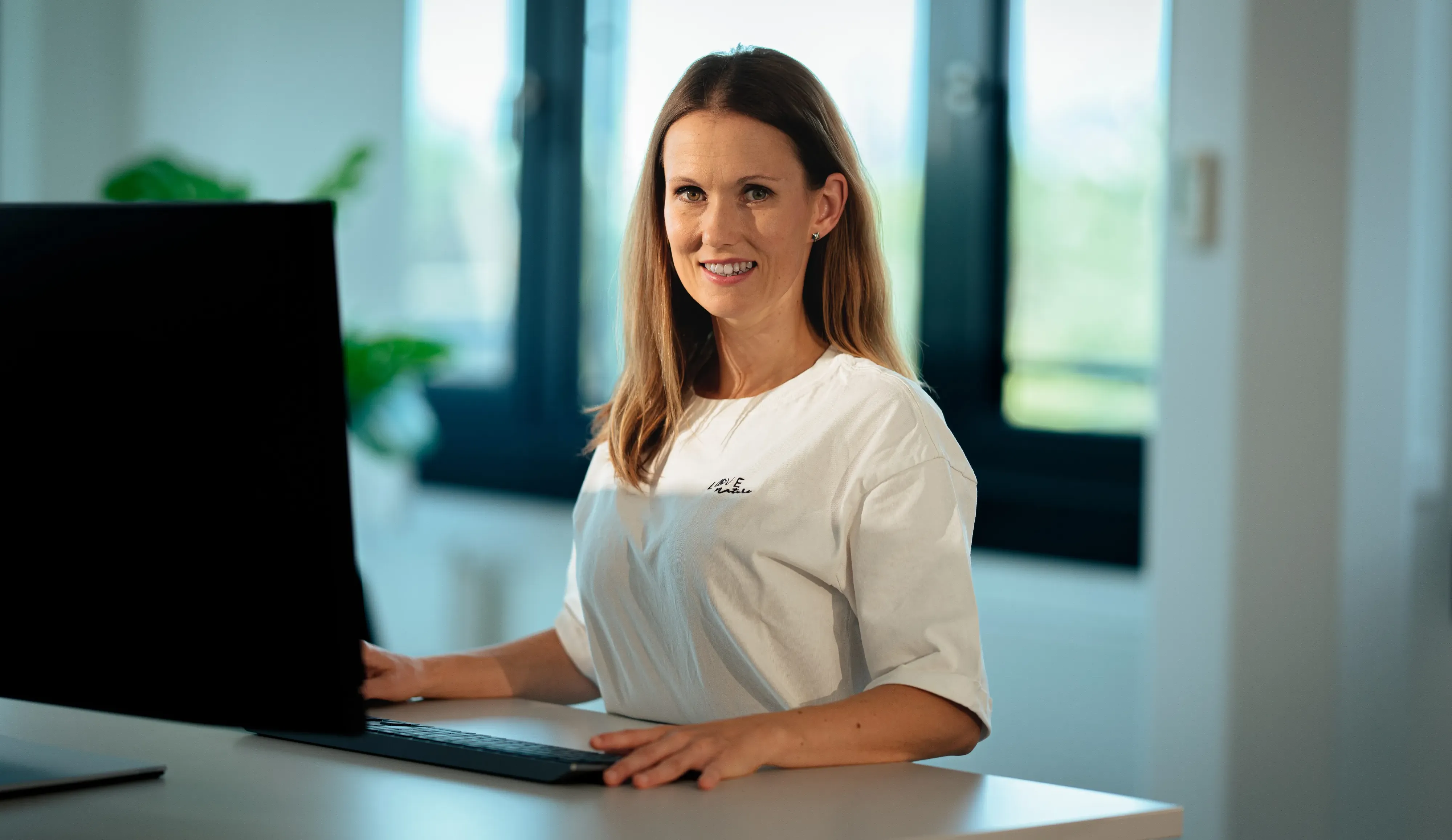 Eine Frau die am PC arbeitet und in die Kamera schaut.