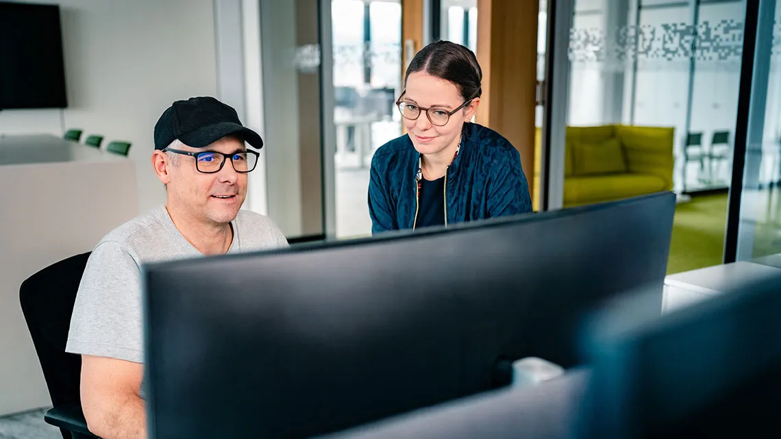 Zwei Personen in einem modernen Büro arbeiten konzentriert an einem Computerbildschirm.