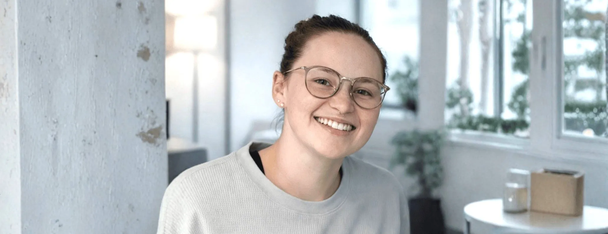 Eine lächelnde junge Frau mit Brille in einem modernen Büro.