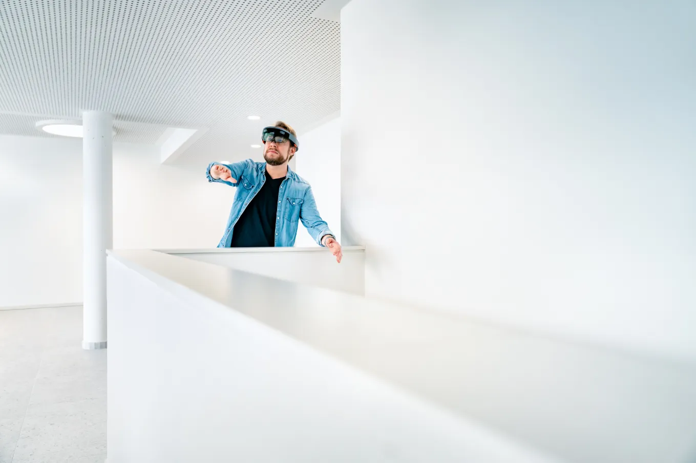 Ein Mann trägt eine AR-Brille und interagiert mit virtuellen Inhalten in einem modernen Bürogebäude.