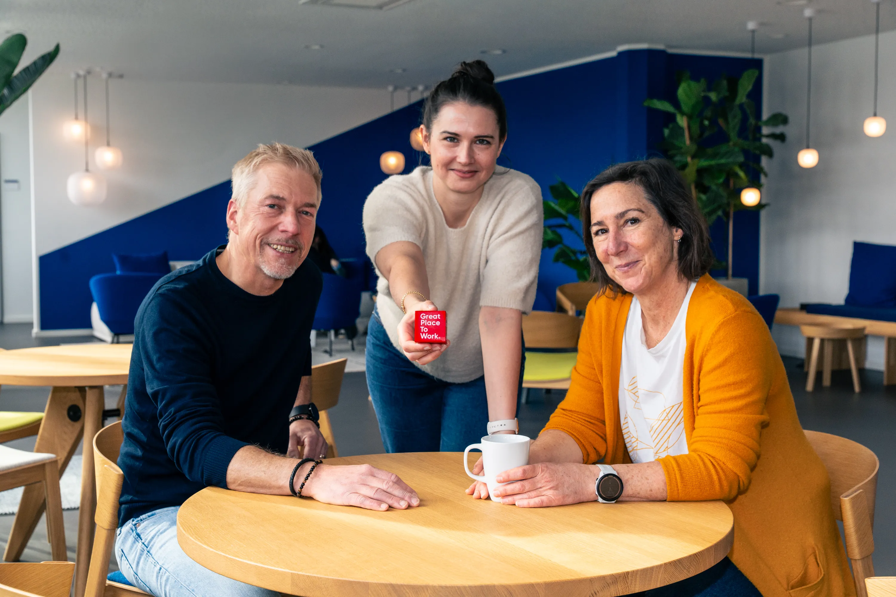 Vier Kollegen diskutieren fröhlich über ein Projekt an einem Laptop auf einer Terrasse.