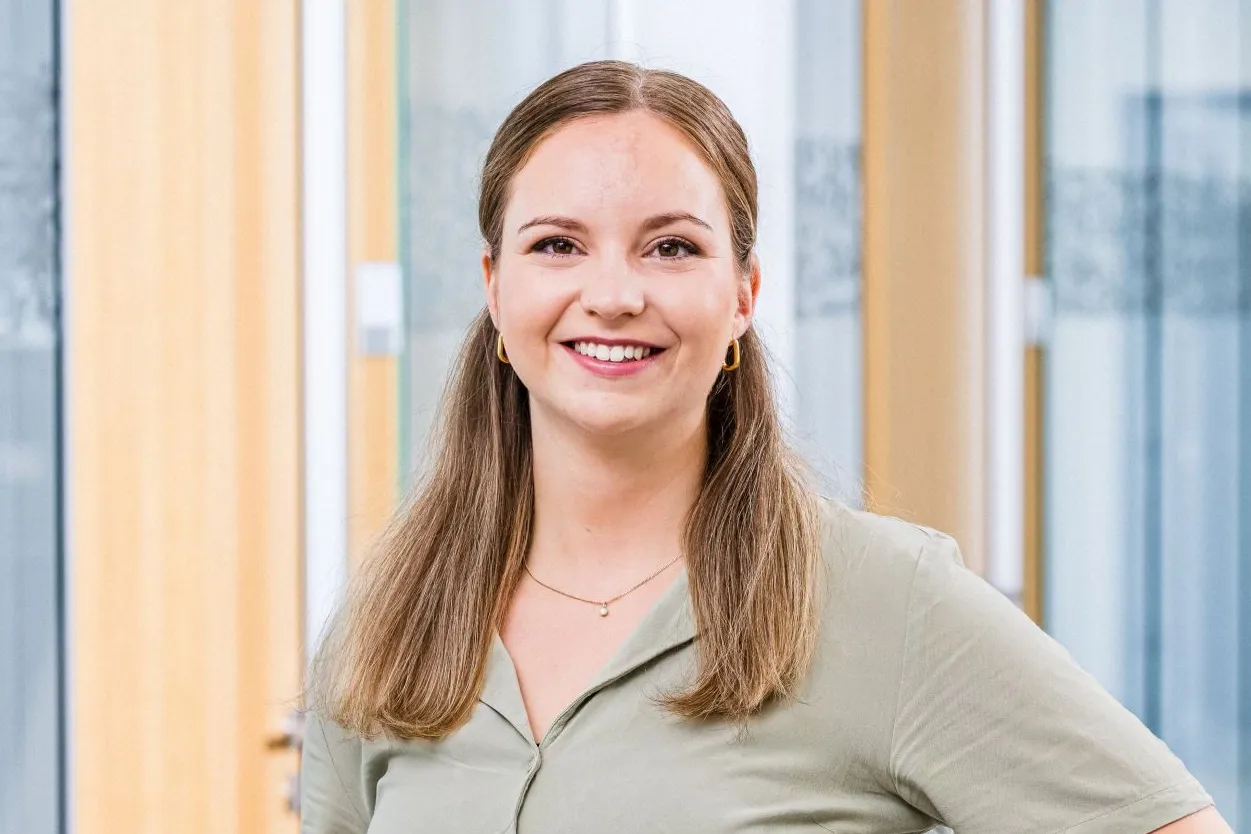 Eine lächelnde Frau steht selbstbewusst in einem modernen Büroflur der Haufe-Group.