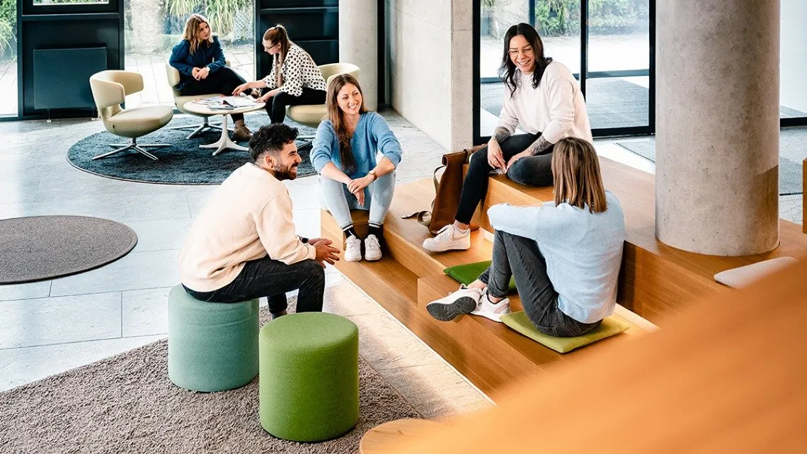 Eine Gruppe von Kollegen sitzt in einem offenen Büro im Kreis und unterhält sich.. 
