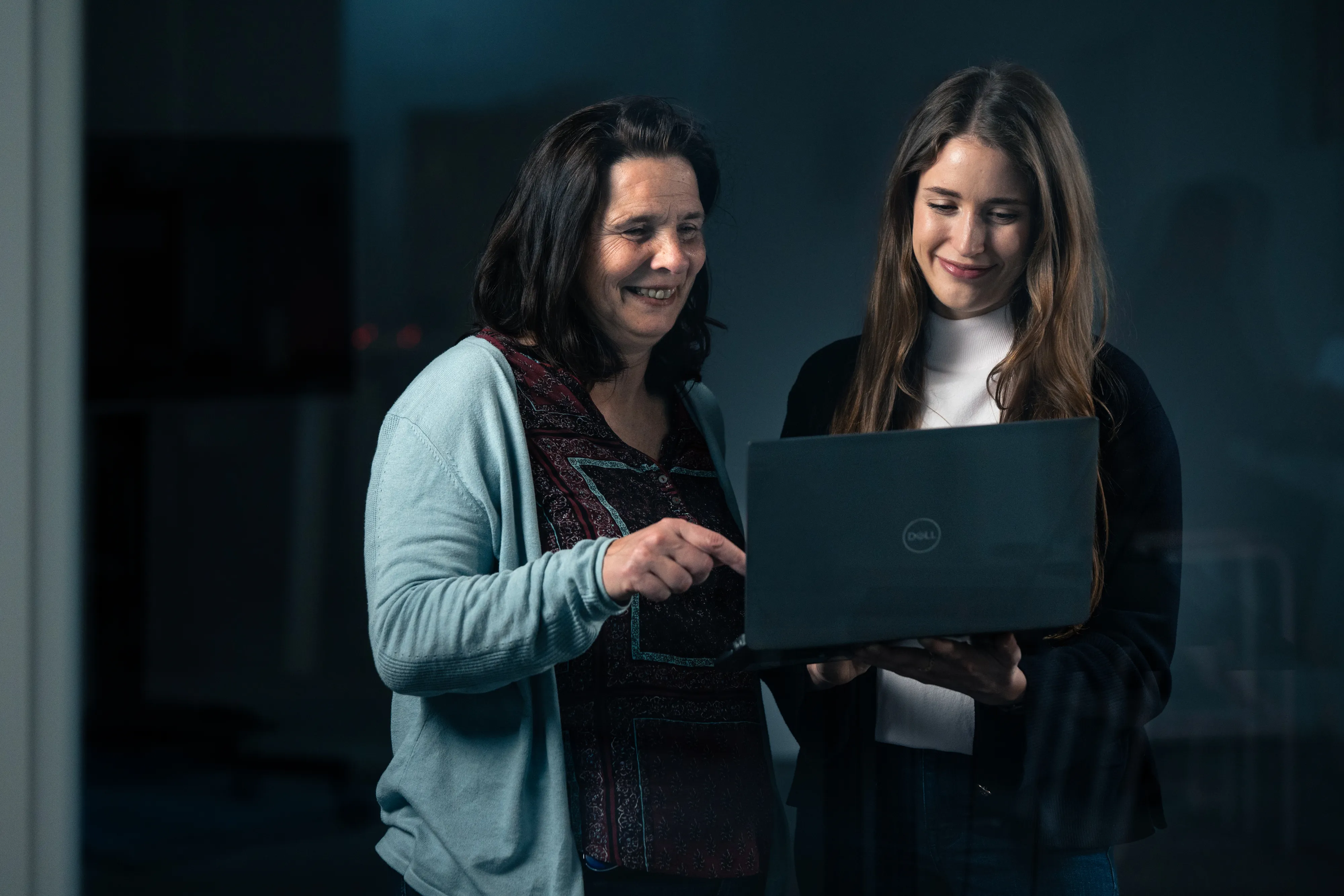 Two colleagues smiling and chatting while looking at a laptop, showing teamwork