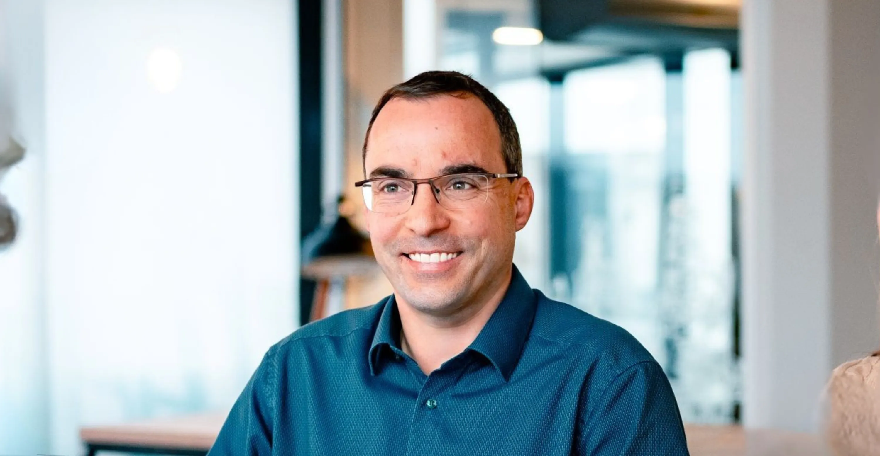 Eine lächelnde Person mit Brille in einem modernen Büro, ideal für die IT-Karriereseite von Haufe-Group.