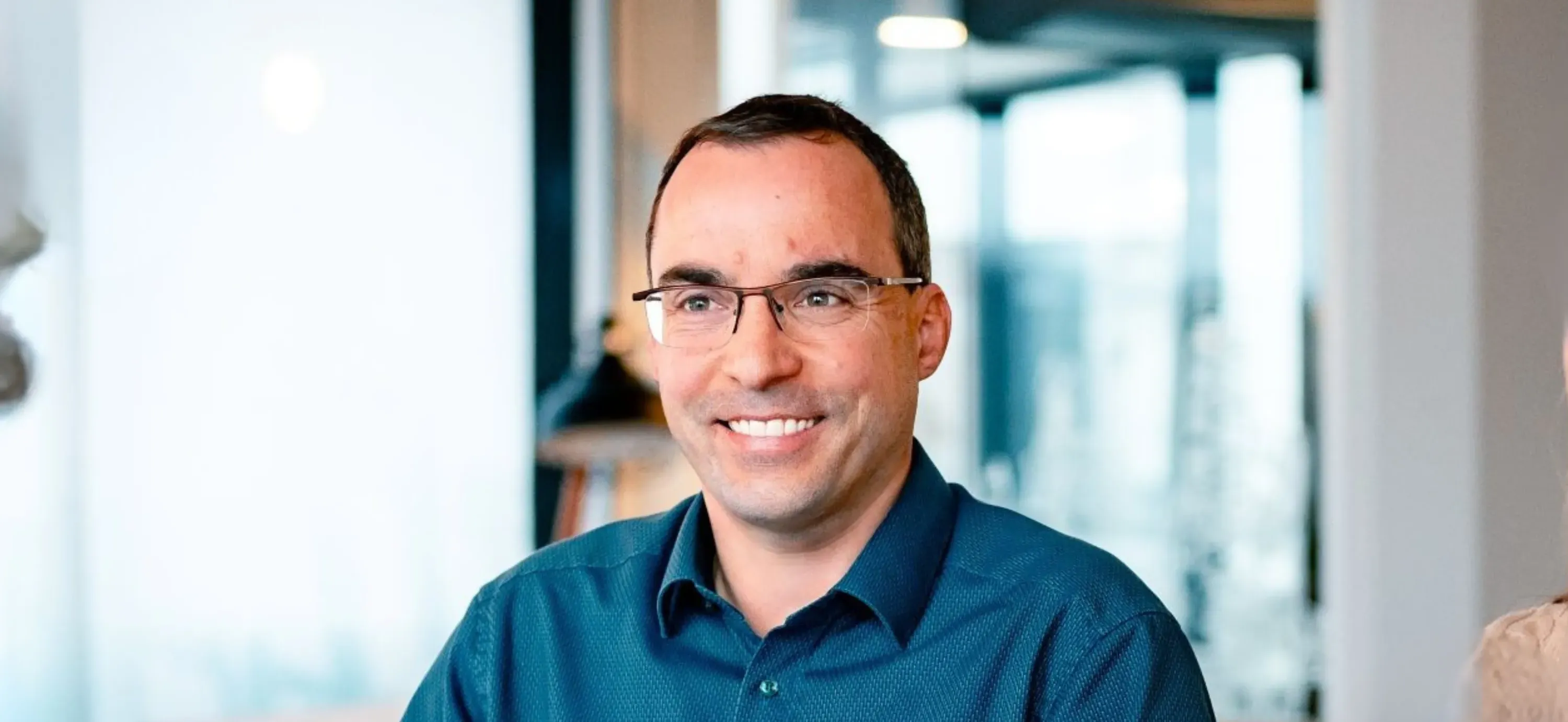 Ein lächelnder Mann mit Brille in einem modernen Büro. Ideal für IT-Karrierewebseiten von Haufe-Group.