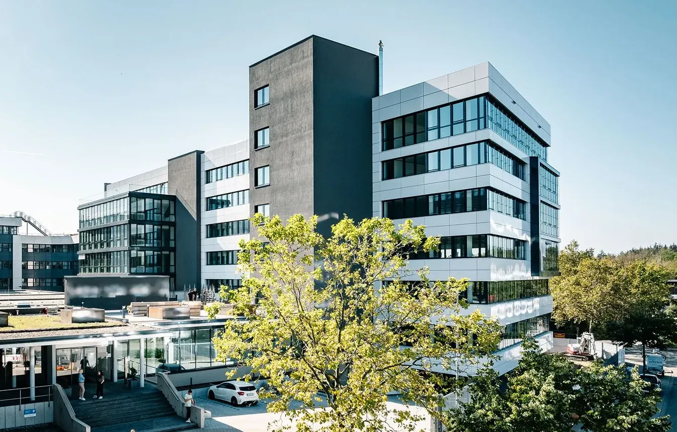 Moderne Bürogebäude mit Glasfassade bei Haufe-Group, ideal für IT-Karrieren. Im Vordergrund Bäume und Autos.
