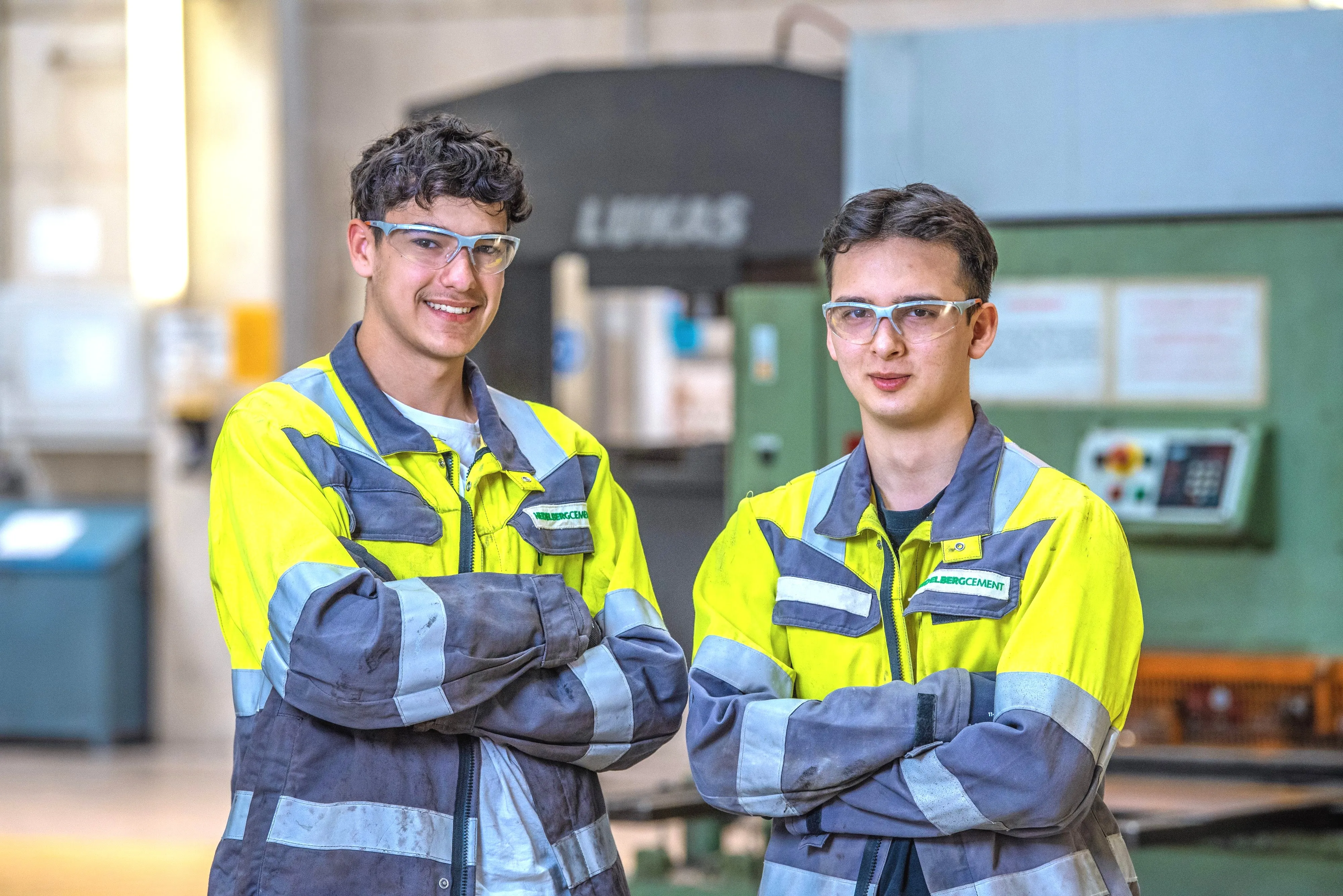 Ein Bauarbeiter in orangefarbener Arbeitskleidung steht vor einem Betonmischer von Heidelberg Materials und lächelt in die Kamera.