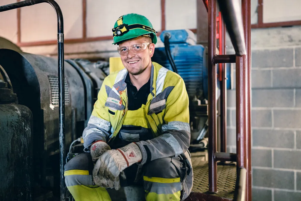 Ein Bauarbeiter in Schutzkleidung und Helm sitzt lächelnd in einer Industrieanlage von Heidelberg Materials.