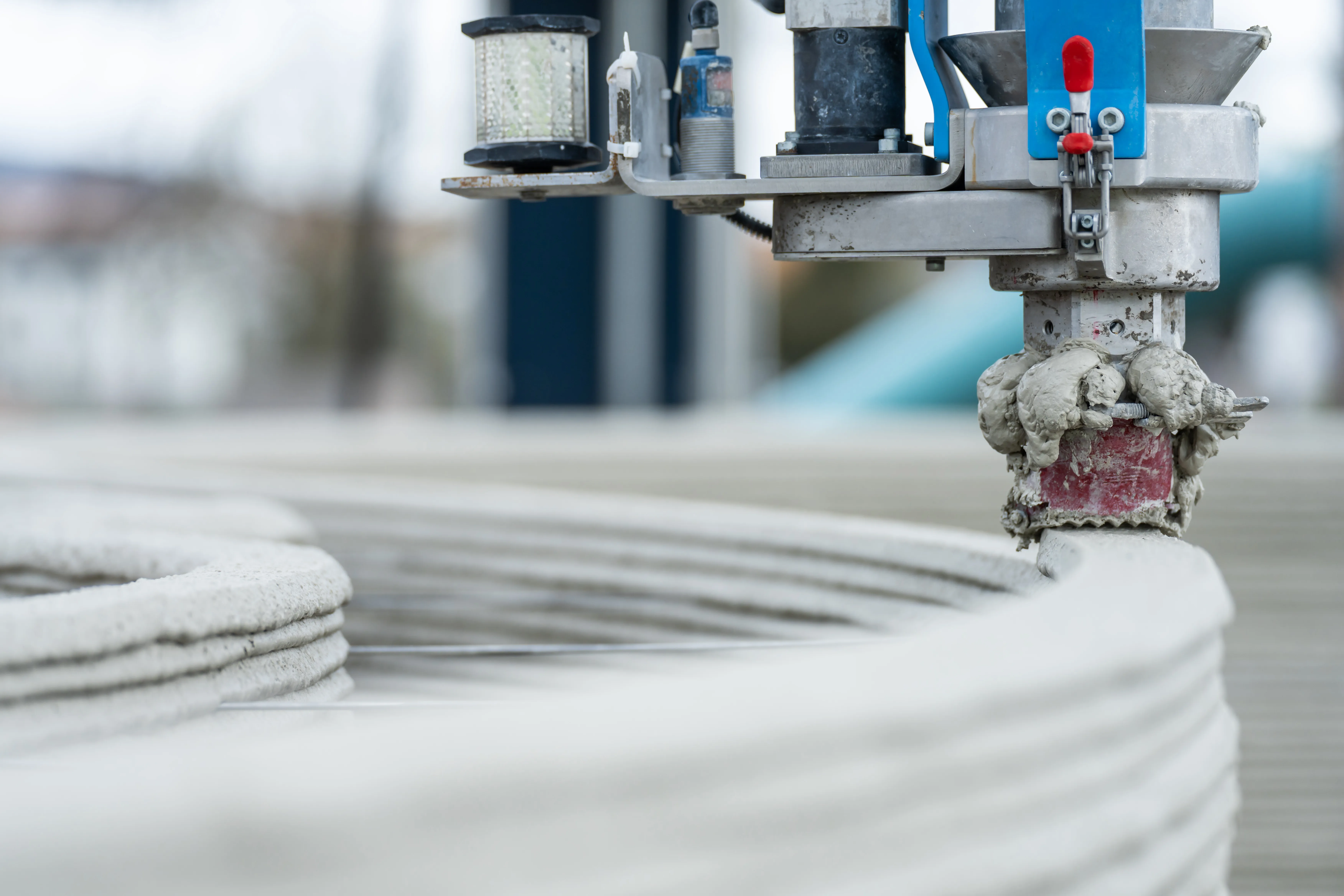 Ein 3D-Drucker trägt Beton auf, um eine Wand zu bauen, was innovative Bauverfahren zeigt.