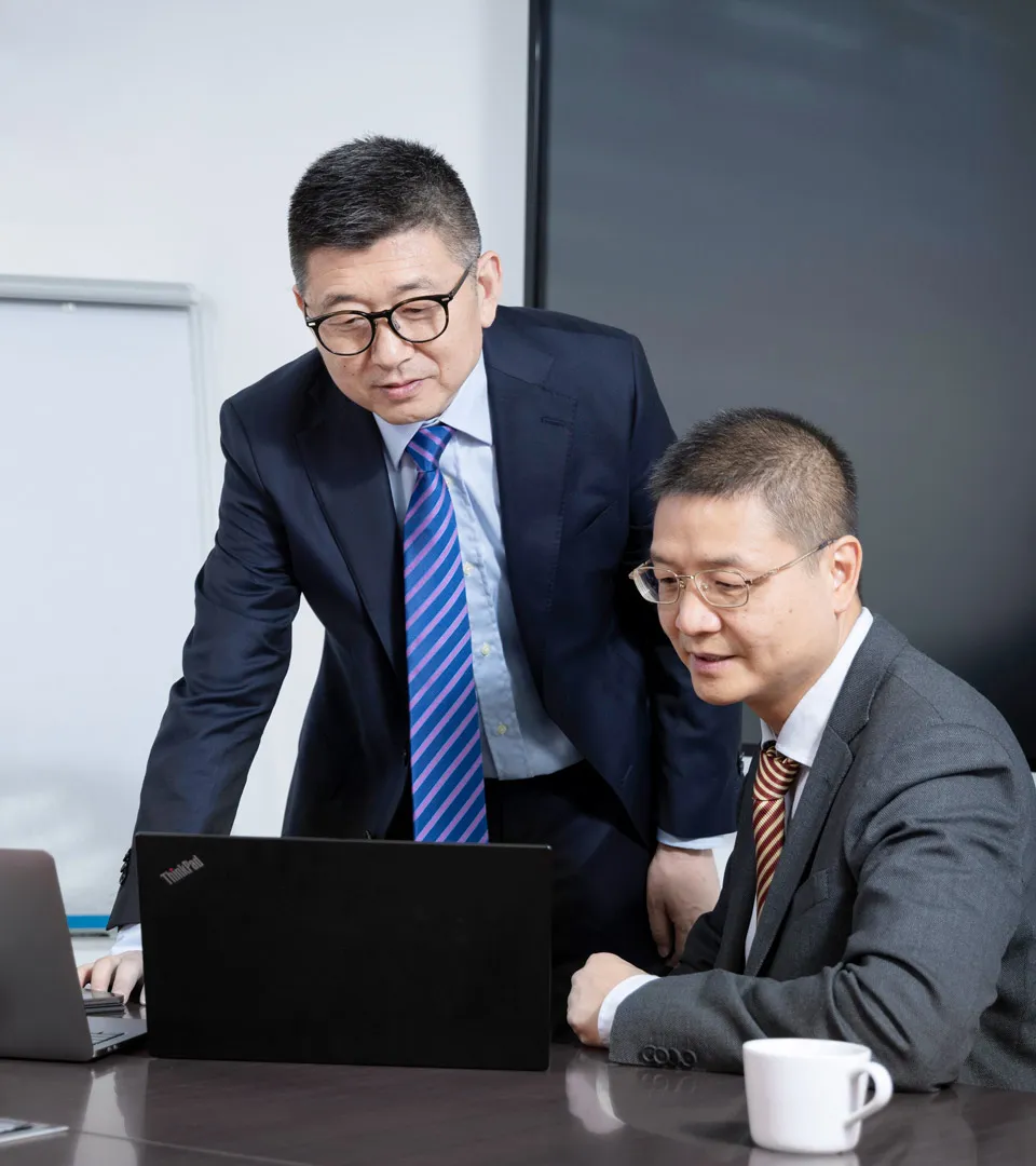 Two colleagues in suits discussing a project on a laptop in a modern office setting at Heitkamp & Thumann.