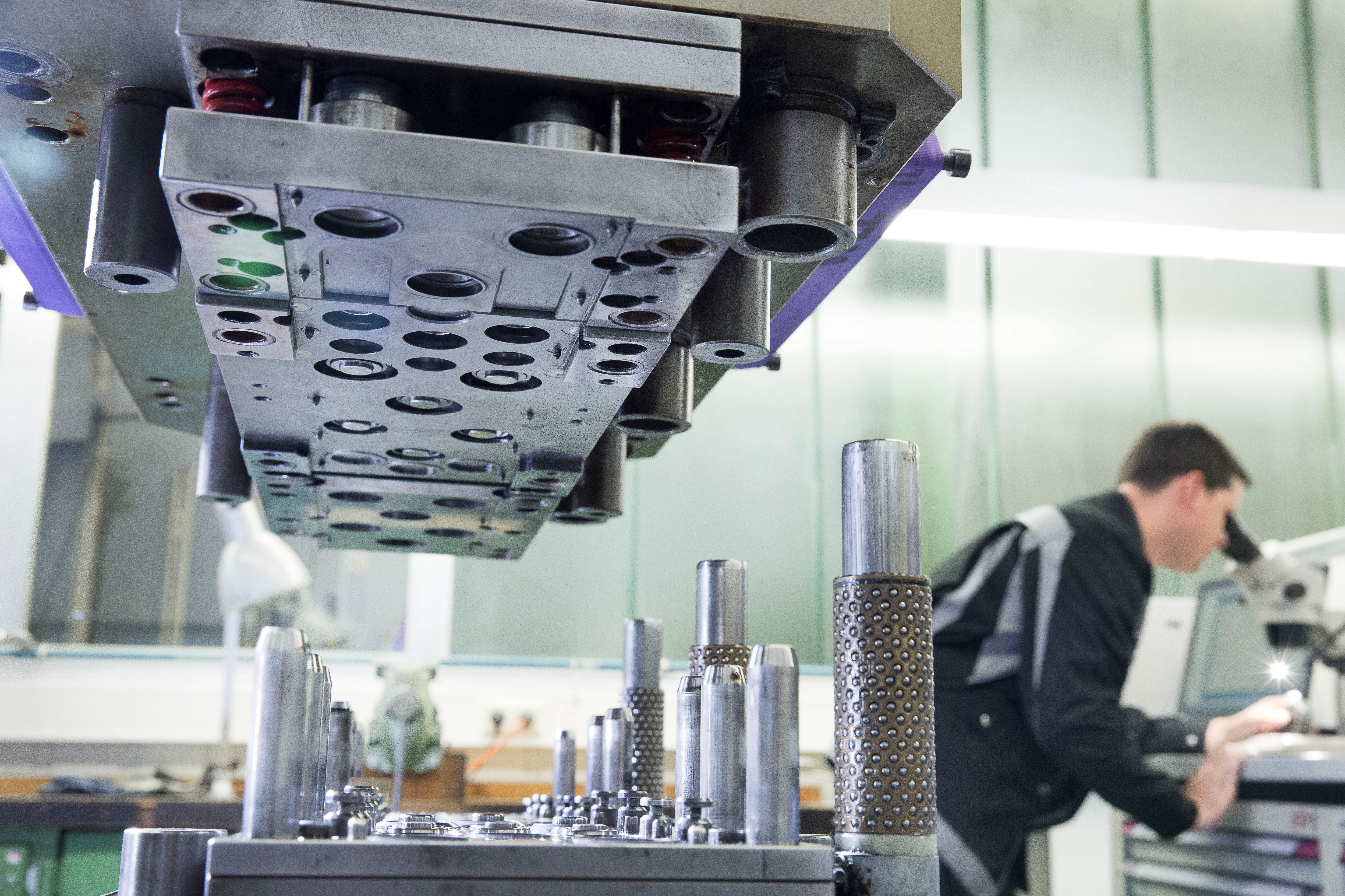 Industrielle Fertigungsanlage mit einem Mitarbeiter, der an einem Mikroskop arbeitet. Perfekt für Deine Karriere bei Heitkamp & Thumann.