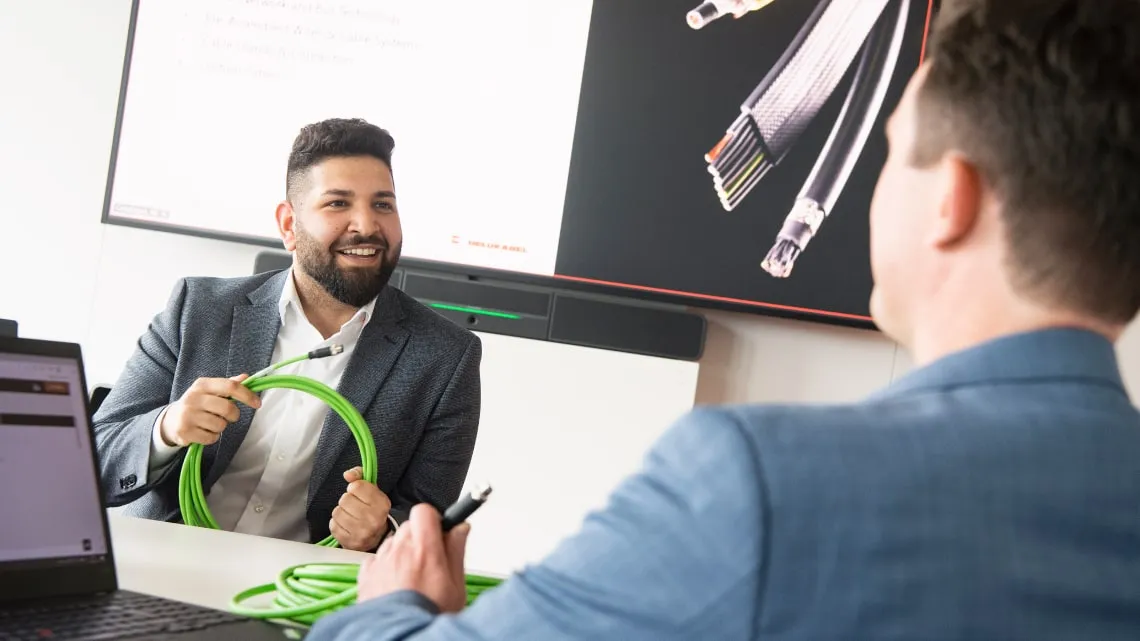 Ein Mitarbeiter von HELU KABEL zeigt einem Kollegen ein grünes Kabel in einem modernen Büro.