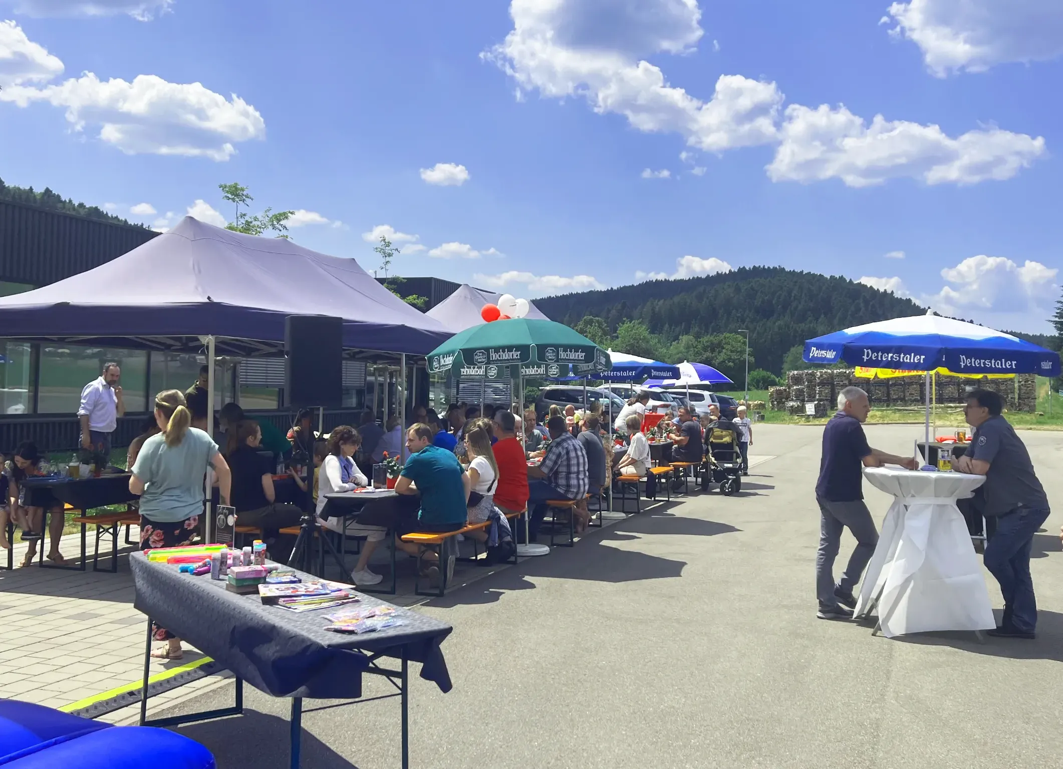 Mitarbeiter von HELU KABEL bei einem Sommerfest im Freien, sitzen an Biertischen unter Pavillons und Sonnenschirmen.