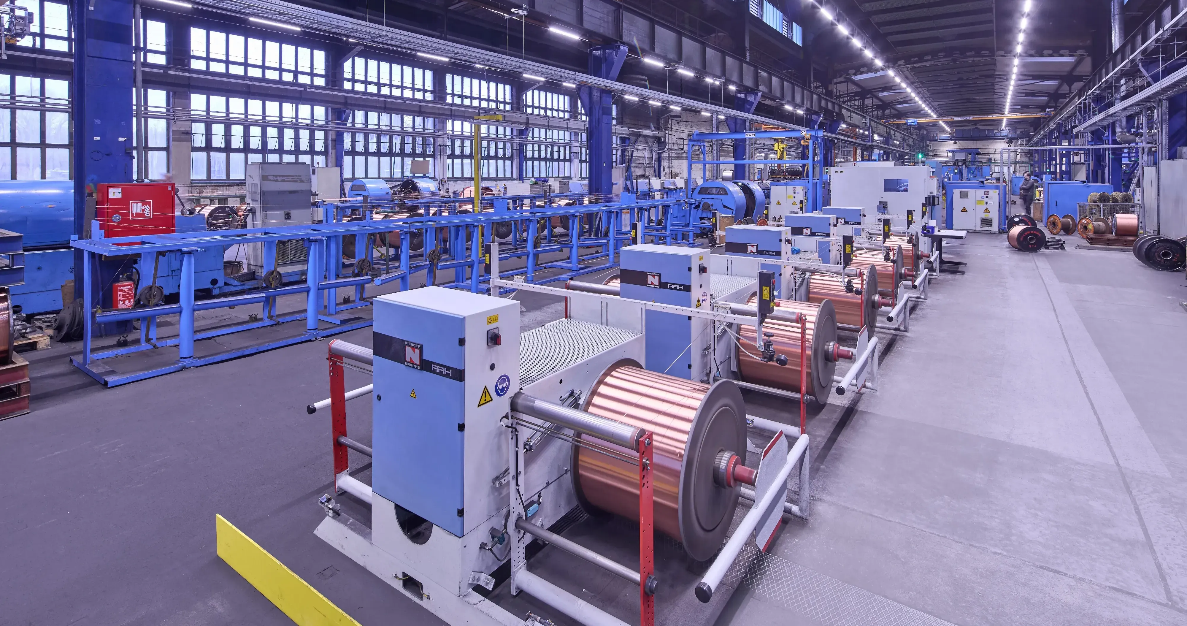 Produktionshalle von HELU KABEL GmbH mit Maschinen zur Kabelherstellung und großen Kabelrollen.