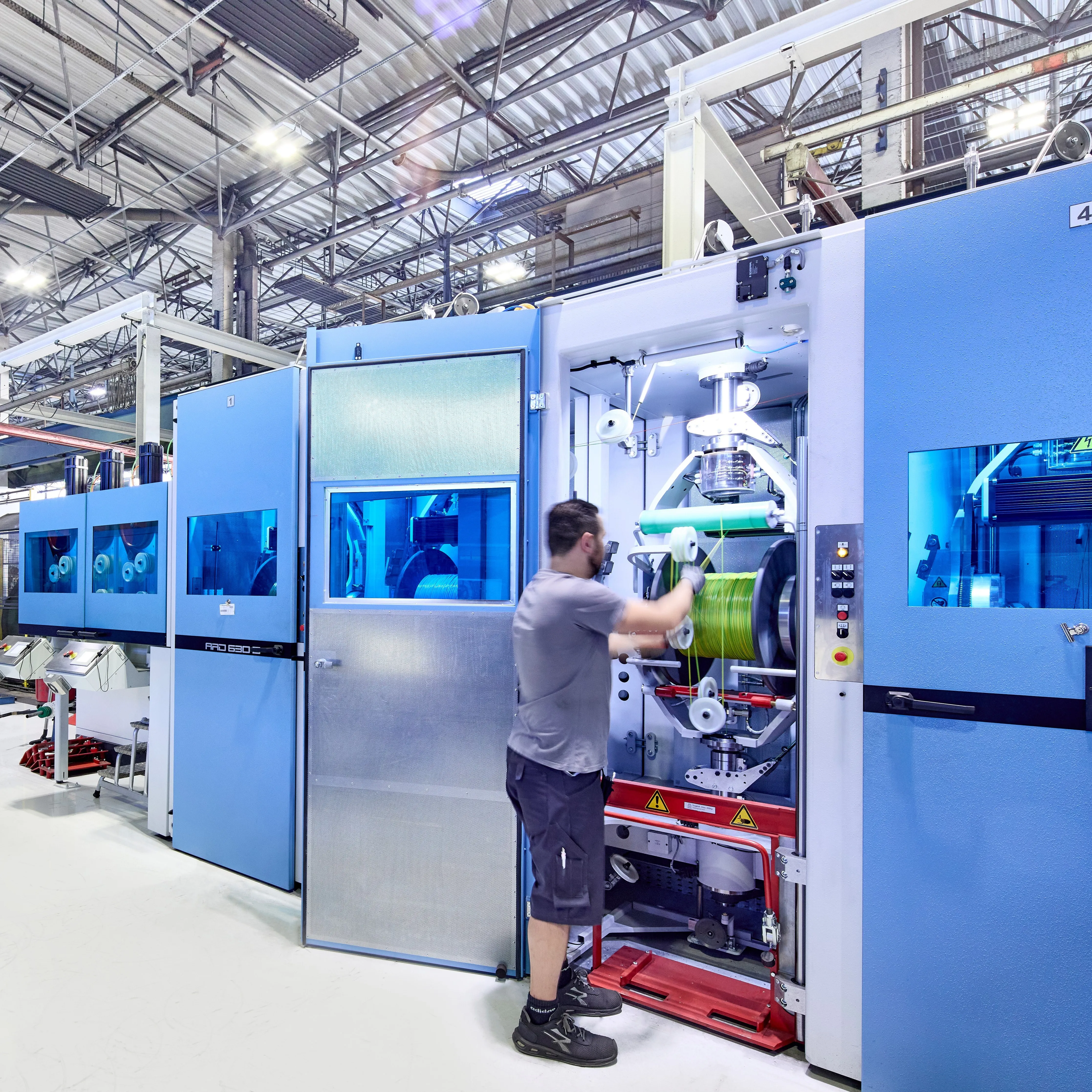Ein Techniker arbeitet an einer modernen Kabelproduktionsmaschine in einer Fabrikhalle bei HELU KABEL GmbH.