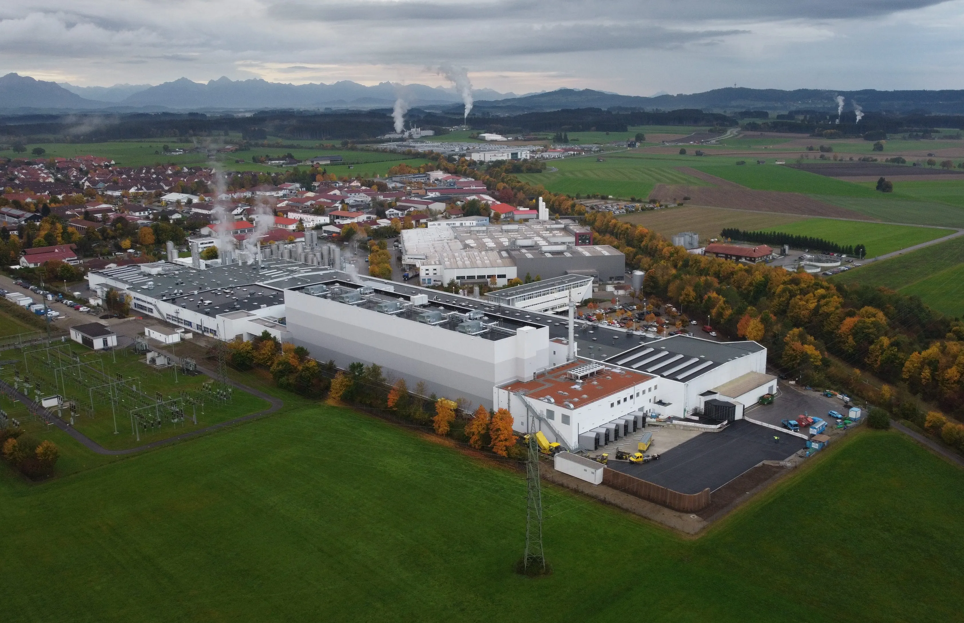 Luftaufnahme eines modernen Lebensmittelwerks, umgeben von Feldern und nahe einer Stadt, ideal für Deine Karriere im Food-Bereich.