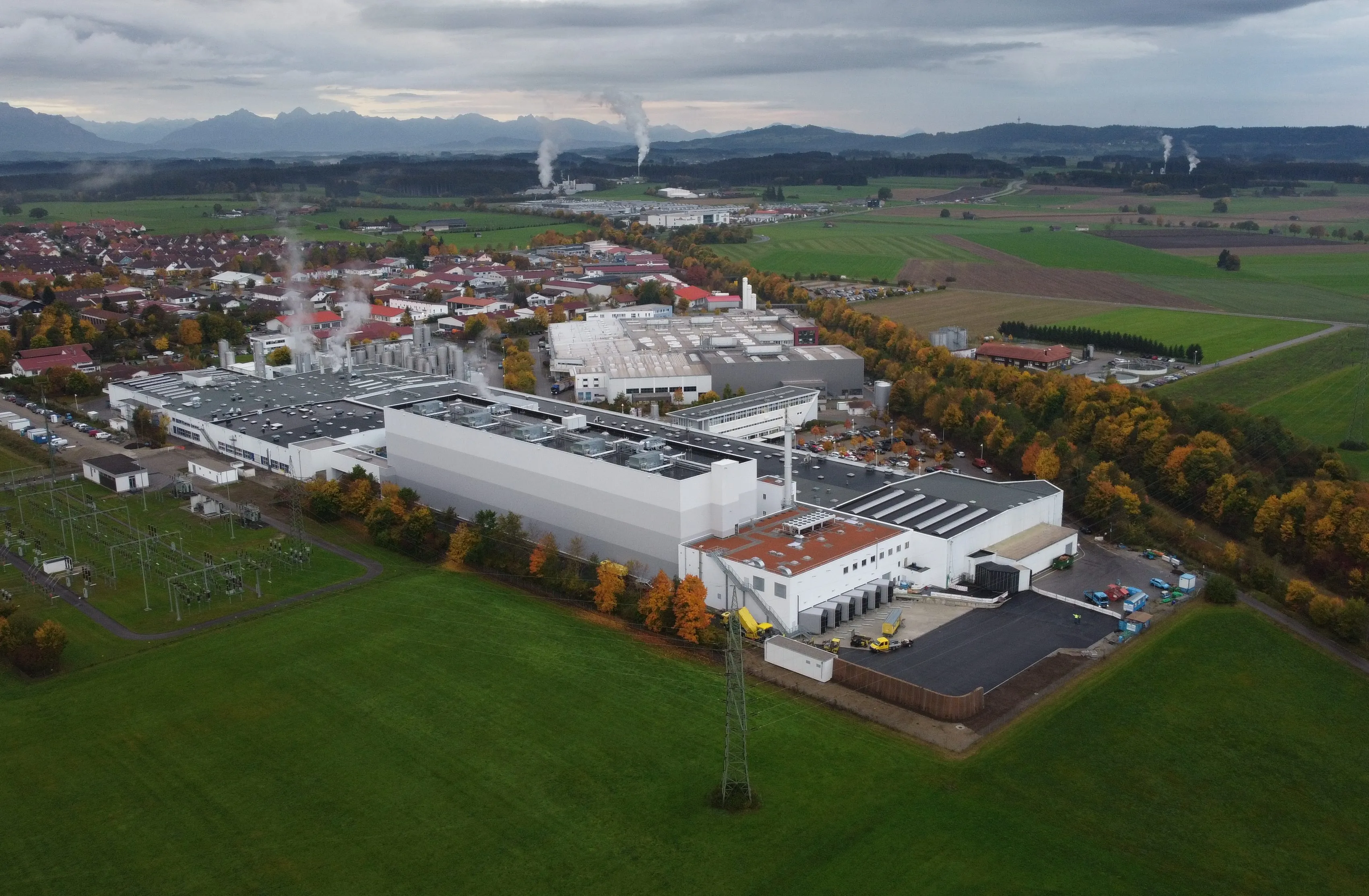 Luftaufnahme eines modernen Lebensmittelwerks, umgeben von Feldern und nahe einer Stadt, ideal für Deine Karriere im Food-Bereich.