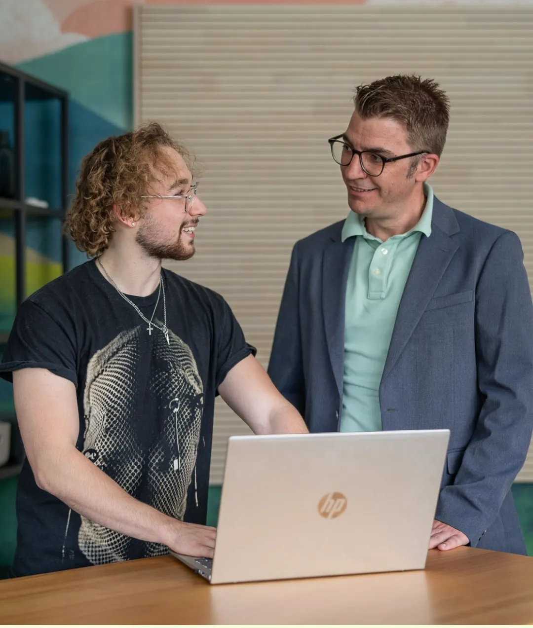 Zwei Kollegen im Gespräch am Laptop, lockere Atmosphäre im Food & Beverage Arbeitsumfeld.