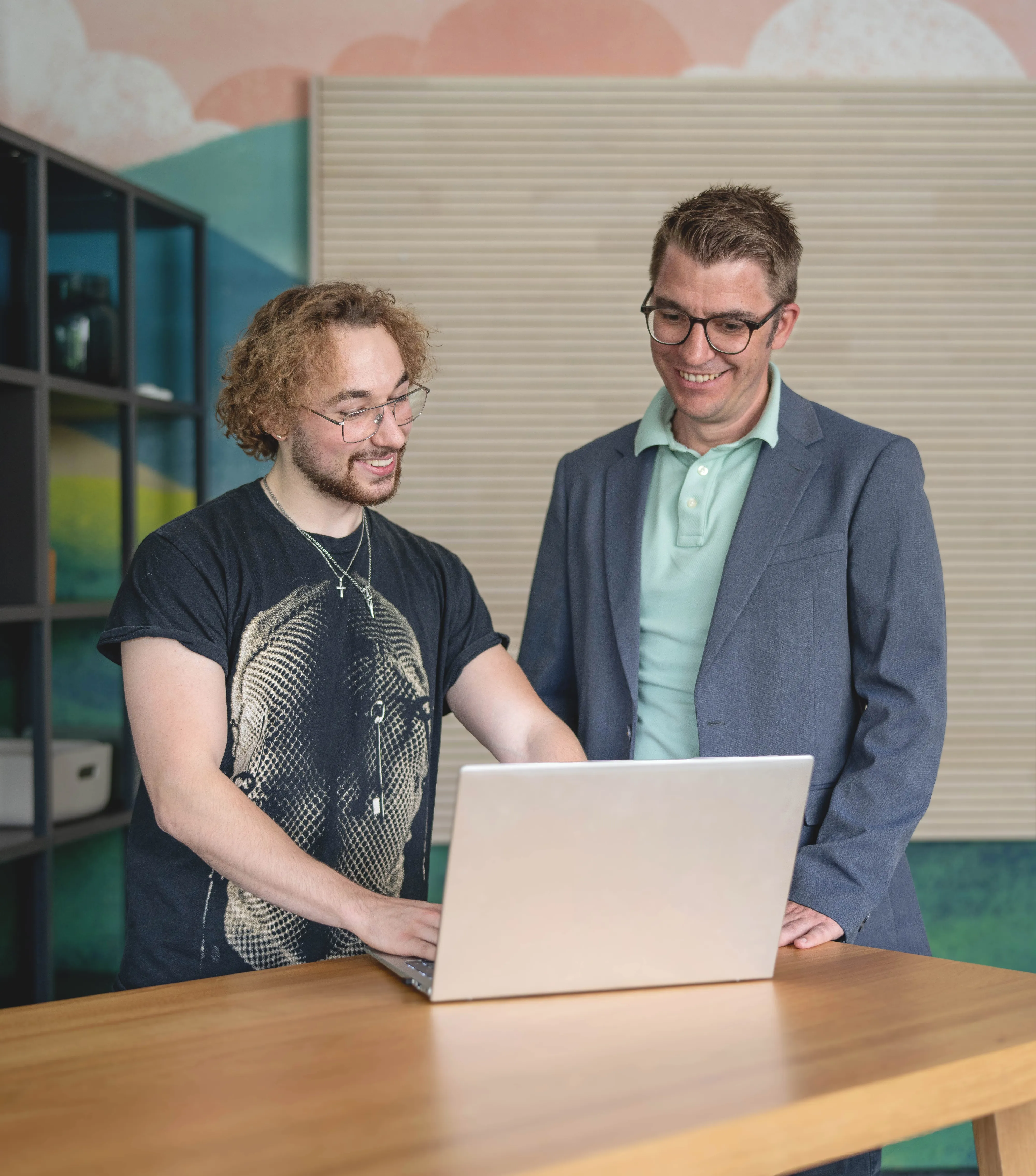 Zwei Kollegen bei Hochland unterhalten sich freundlich am Laptop in einem modernen Büro.